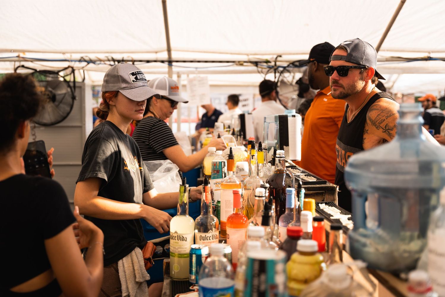 Bartenders serve drinks at outdoor event with various bottles on display.