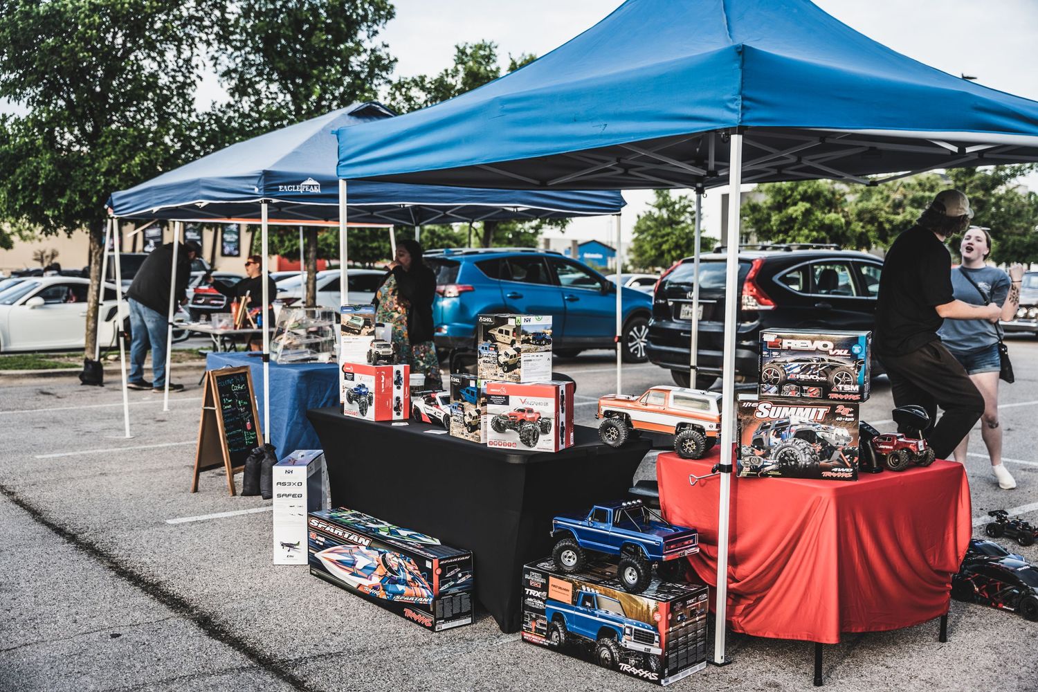 Multiple blue pop-up tents with vendor tables displaying collectible items in a parking lot.