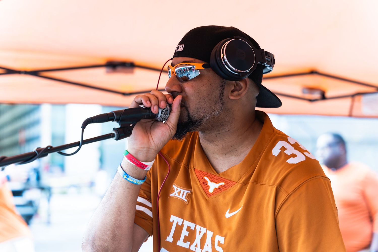 Singer performing with microphone wearing Texas Longhorns jersey and baseball cap under orange tent.