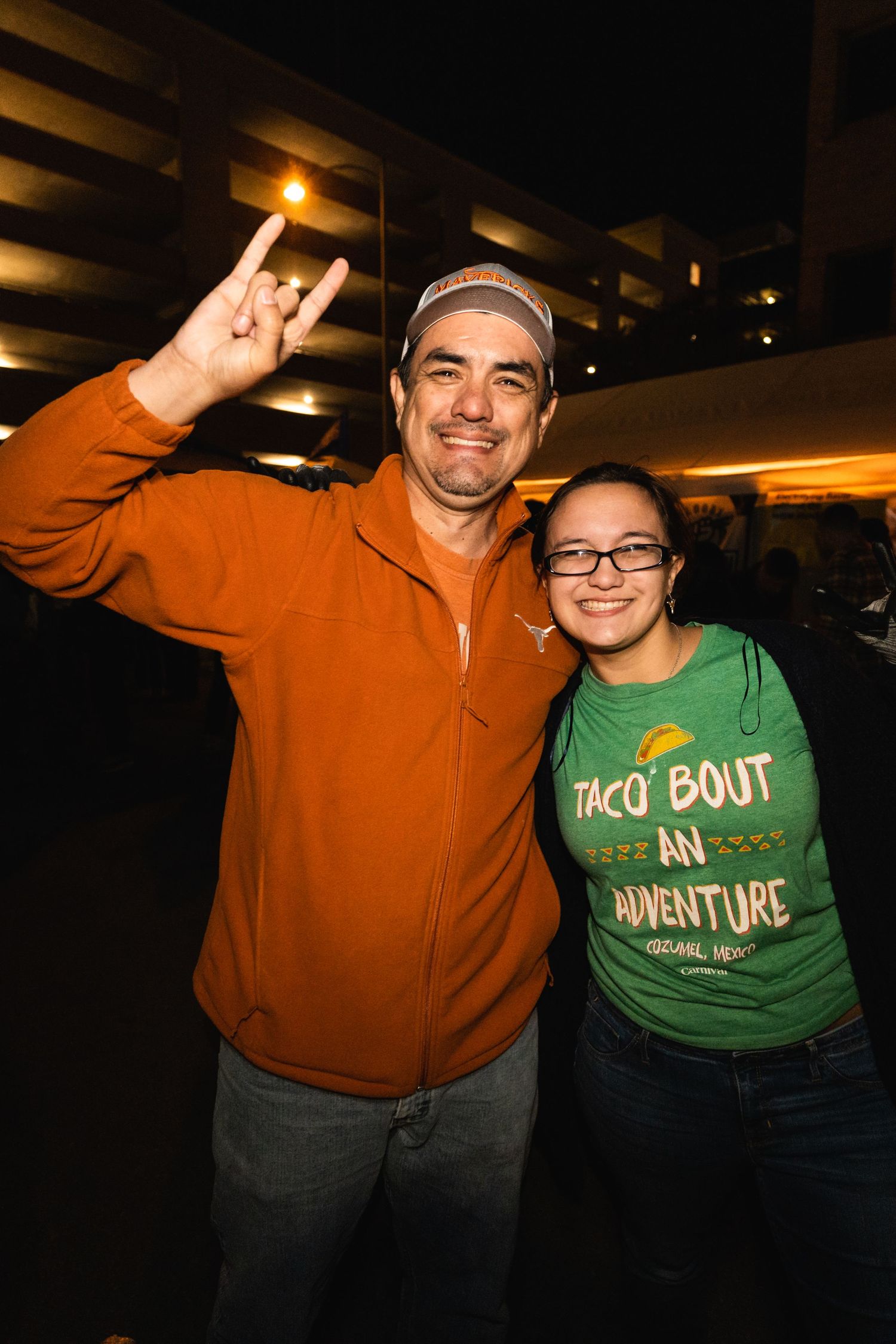 Two attendees in orange and green attire posing together at a nighttime event.