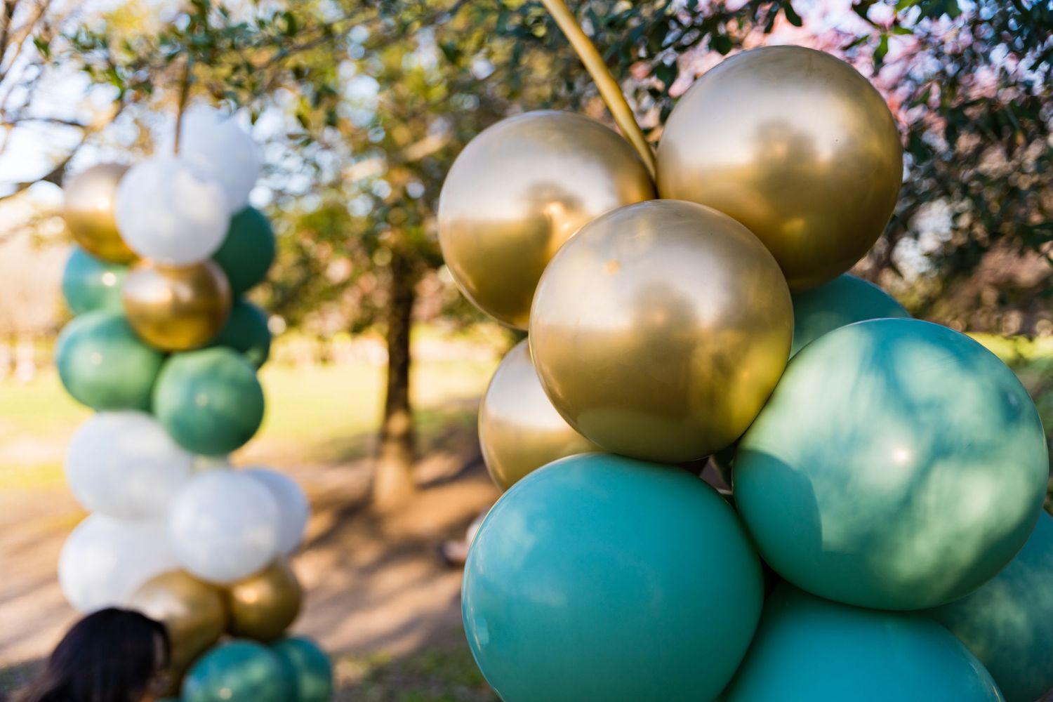 Close-up of metallic gold and teal balloon arch decorations outdoors.