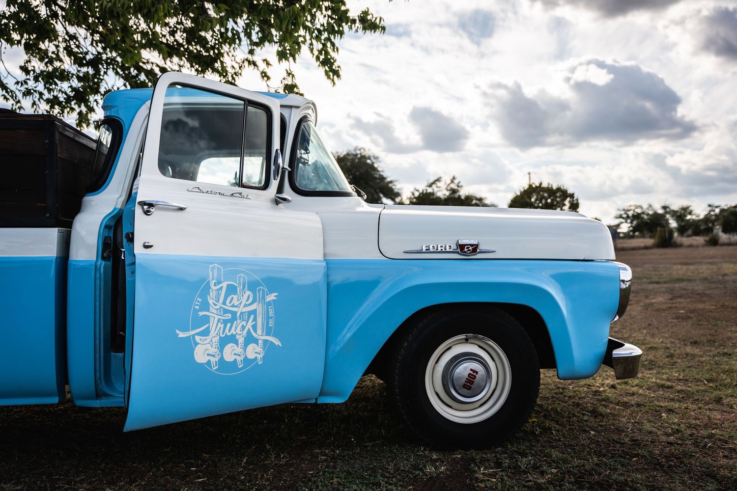 A vintage blue and white pickup truck photographed against a cloudy sky.