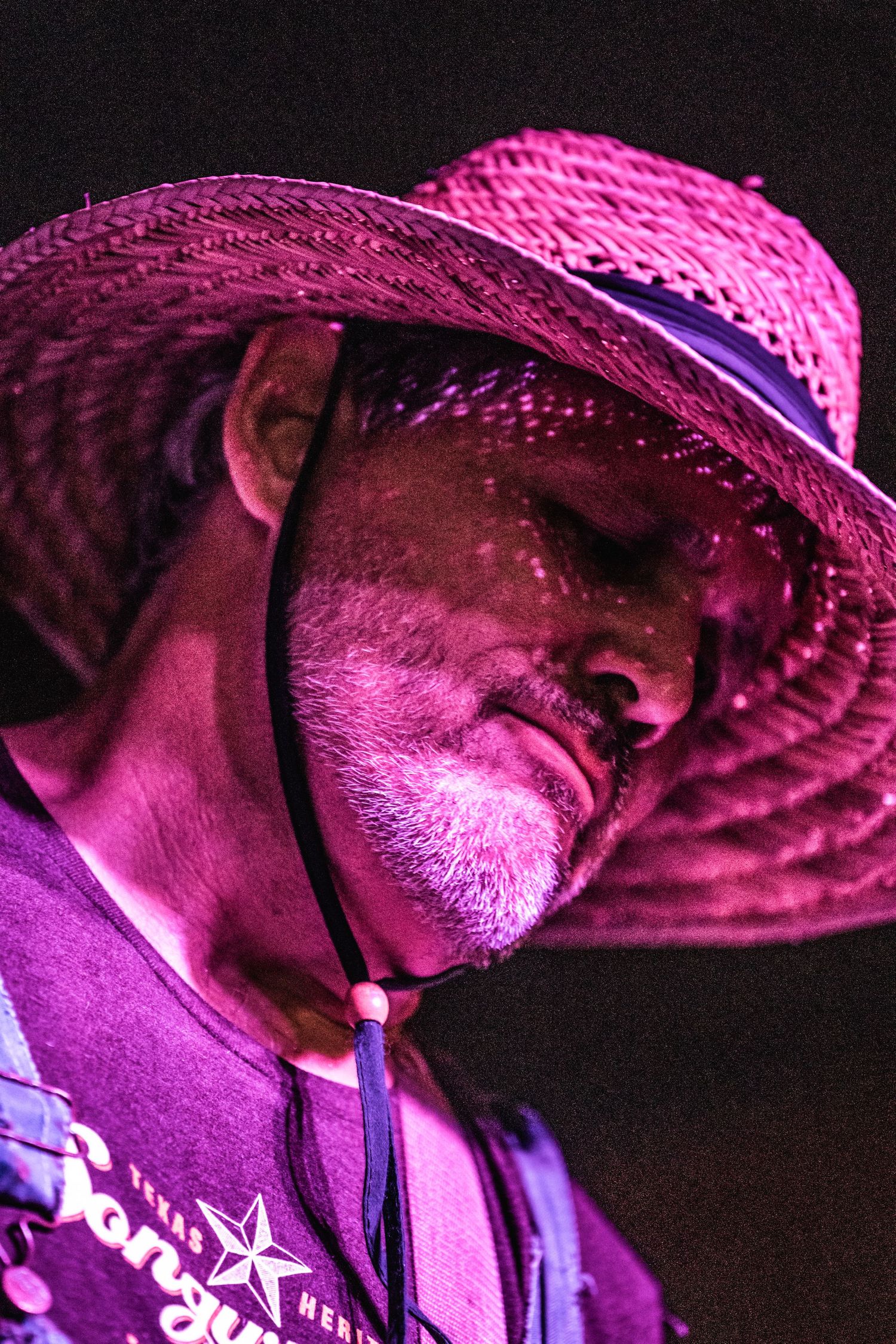 Performer in pink straw hat illuminated by vibrant magenta stage lighting during concert.