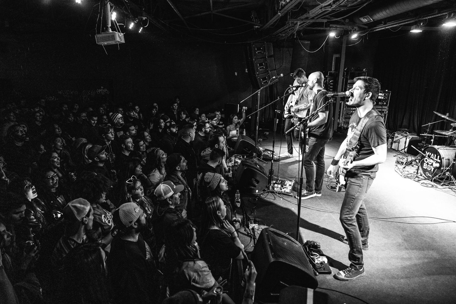 Band performs on elevated stage with crowd watching in black and white photography.