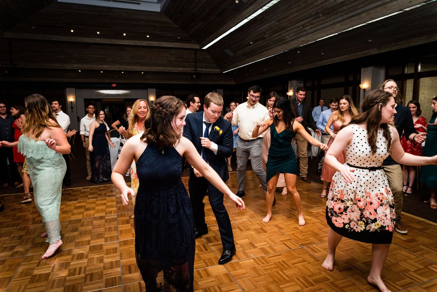Wedding guests dancing and celebrating on a parquet dance floor at a reception.
