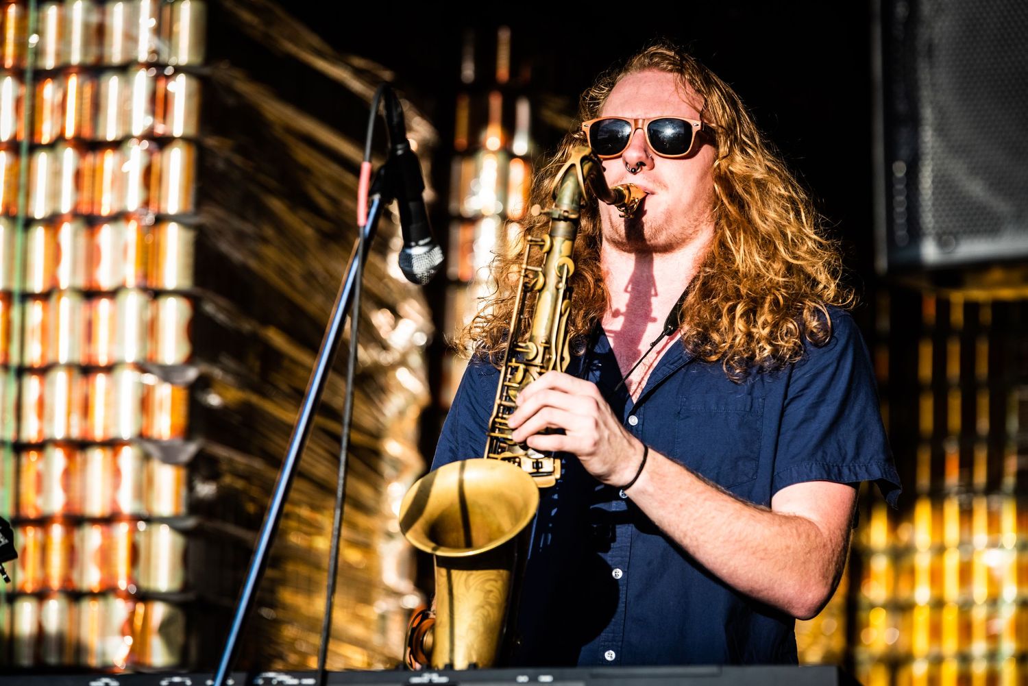 Saxophone player performs on stage with long hair and sunglasses.