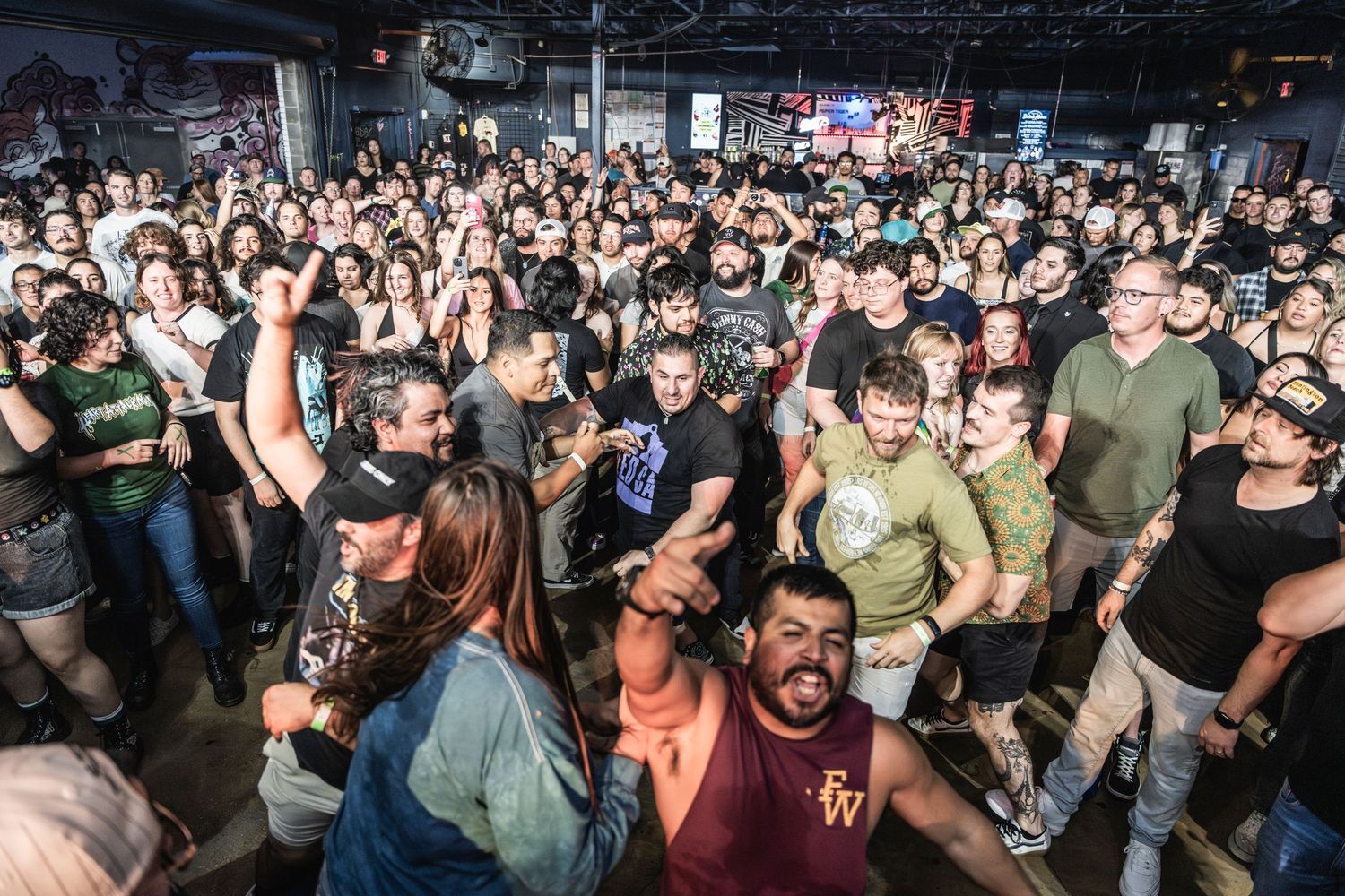 A packed crowd of excited concert-goers fills a dark indoor music venue during a live performance.