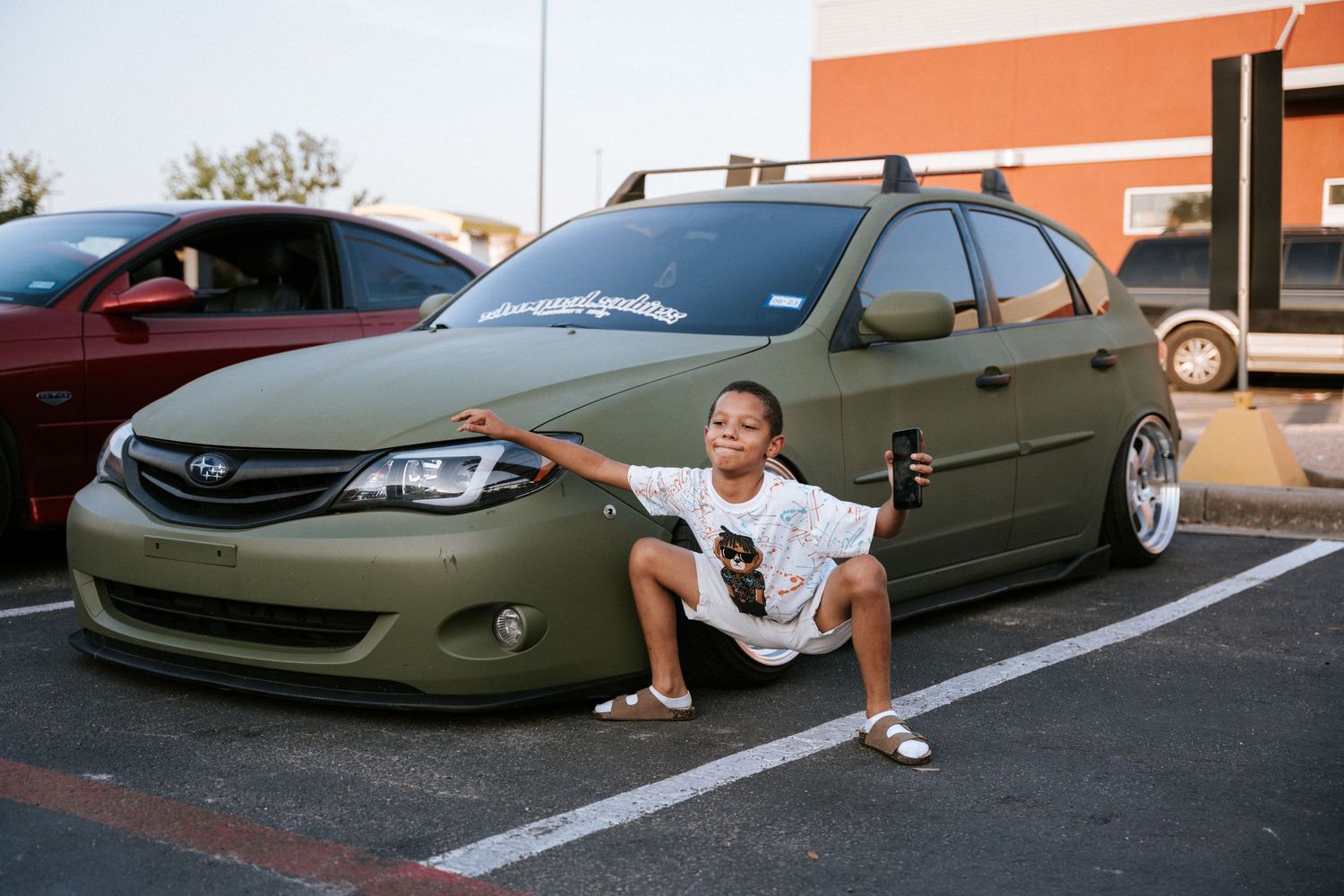 A lowered olive green Subaru sedan parked in a lot with custom aftermarket wheels.