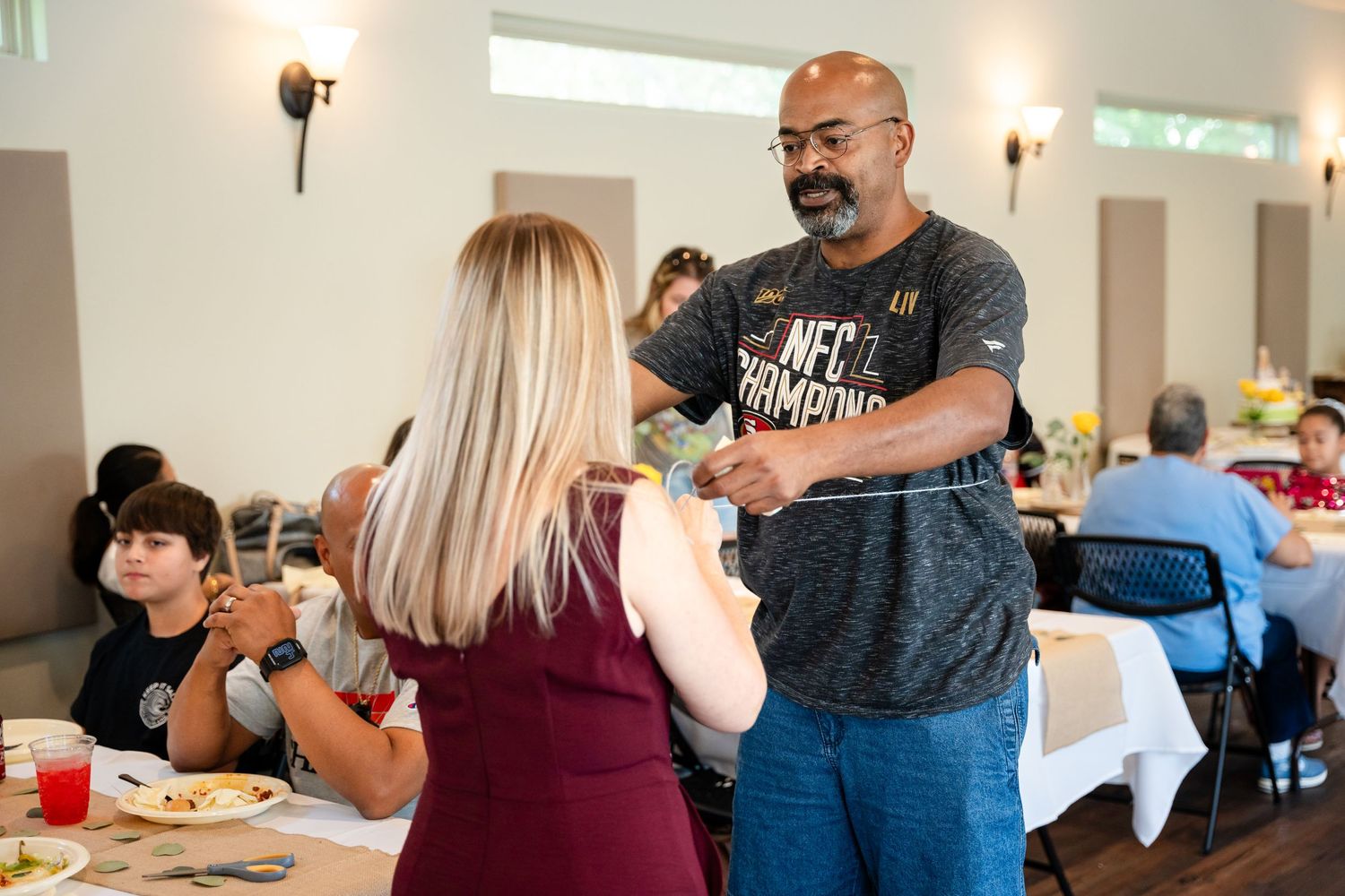 Casual indoor gathering with guests conversing around decorated tables.