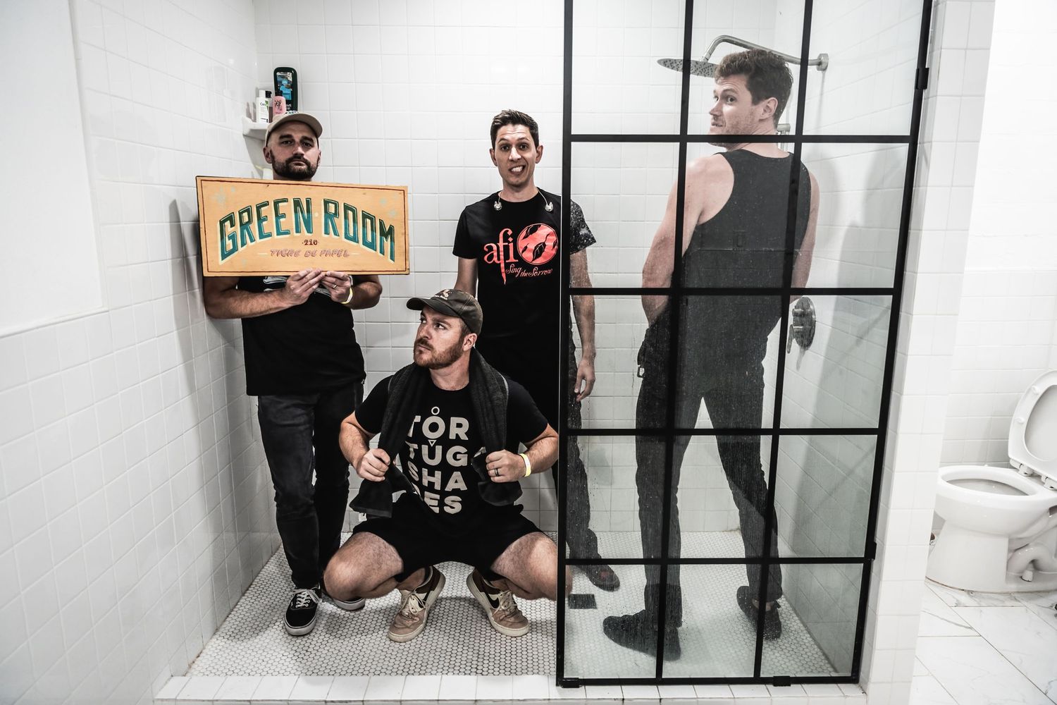Band members pose in a white room holding a Green Room sign.