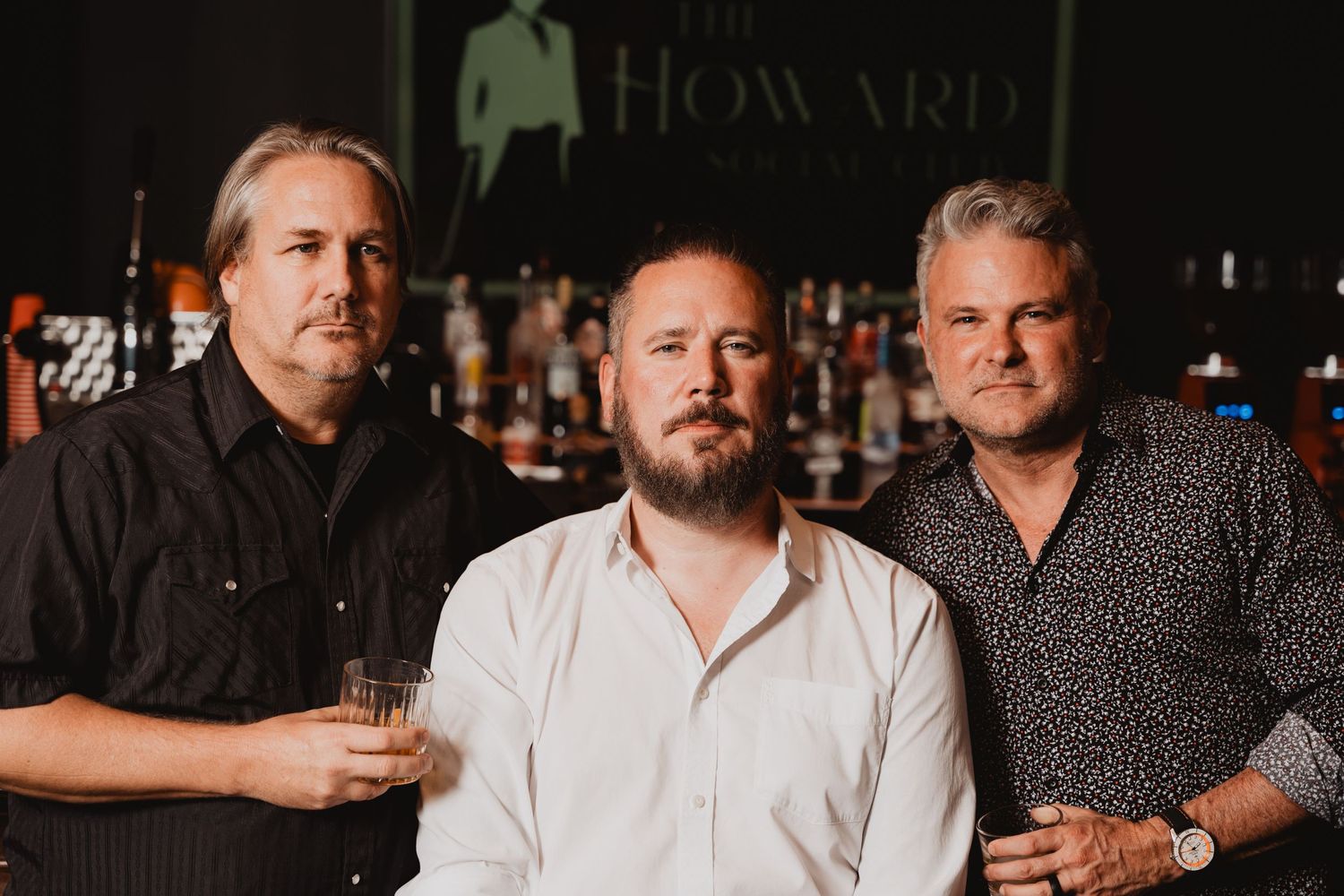 Three people posing in front of illuminated bar shelving with Howard branding.