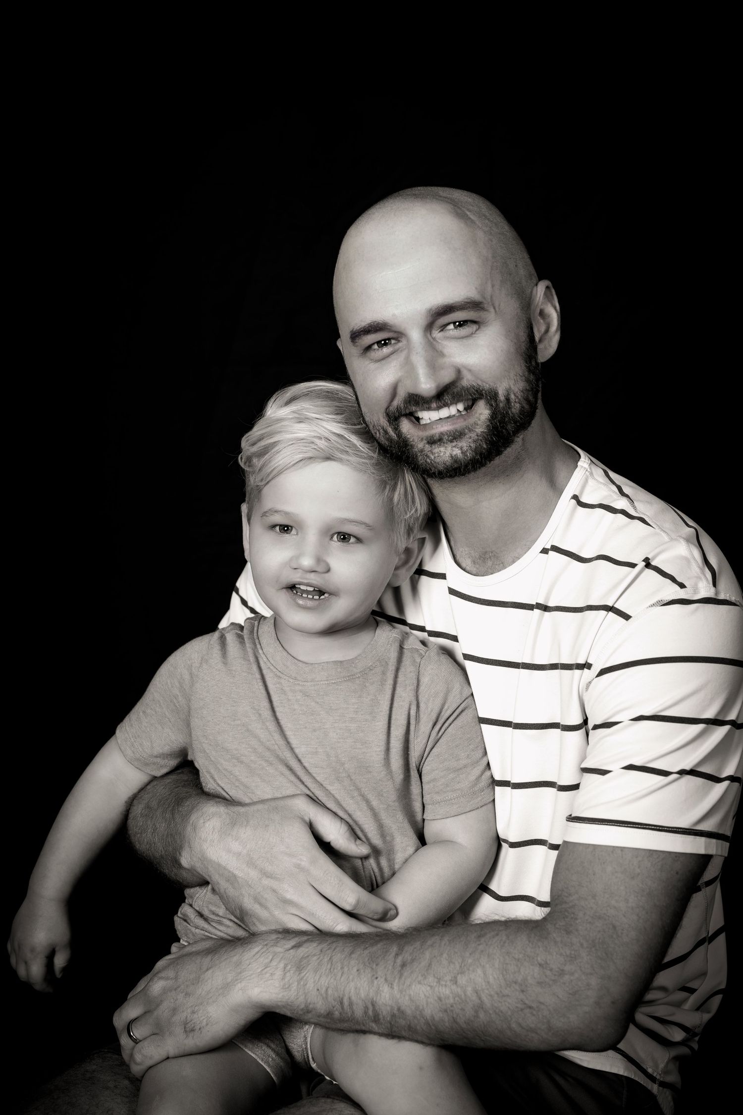 Warm black and white studio portrait showing close family bond and genuine smiles.