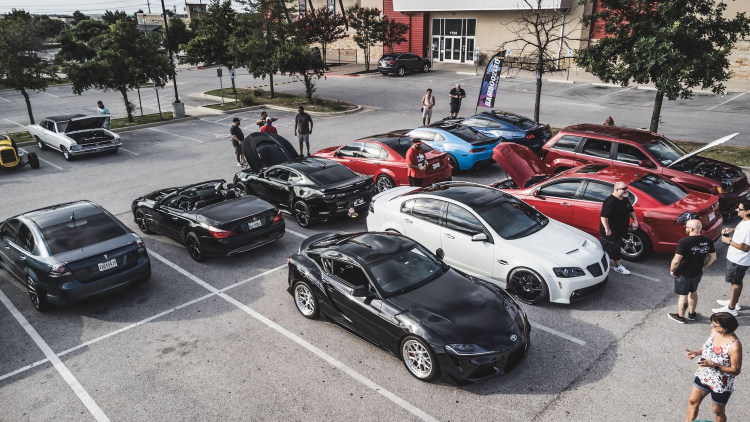 Modern and classic cars displayed at an automotive meetup in a parking lot.