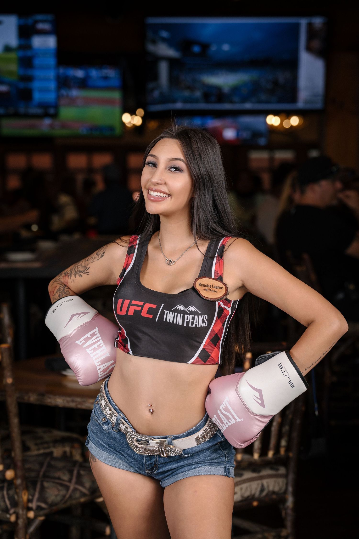 Model wearing UFC gear and pink boxing gloves poses with confident smile.