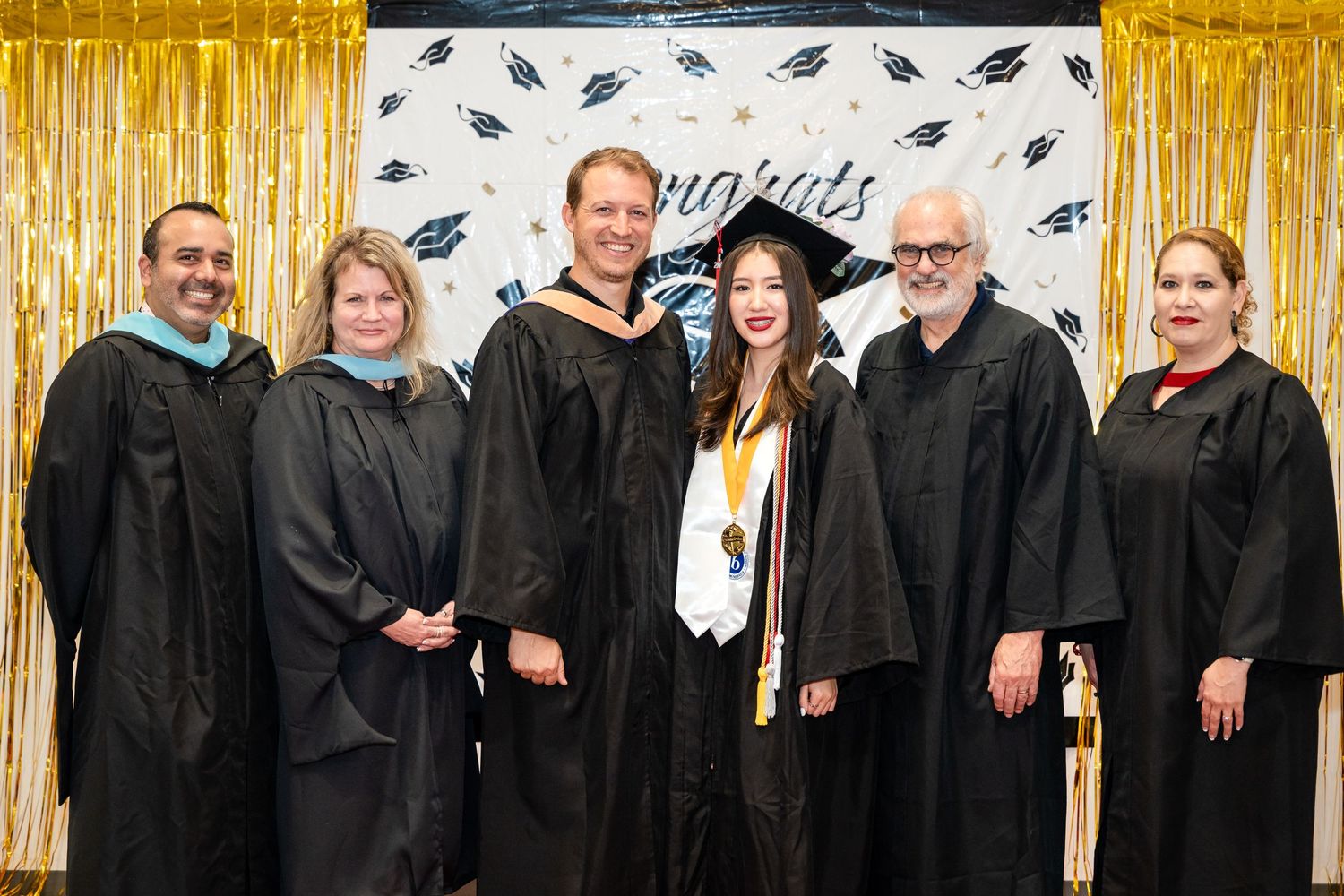 Group photo of graduates and faculty in black robes against a gold backdrop.