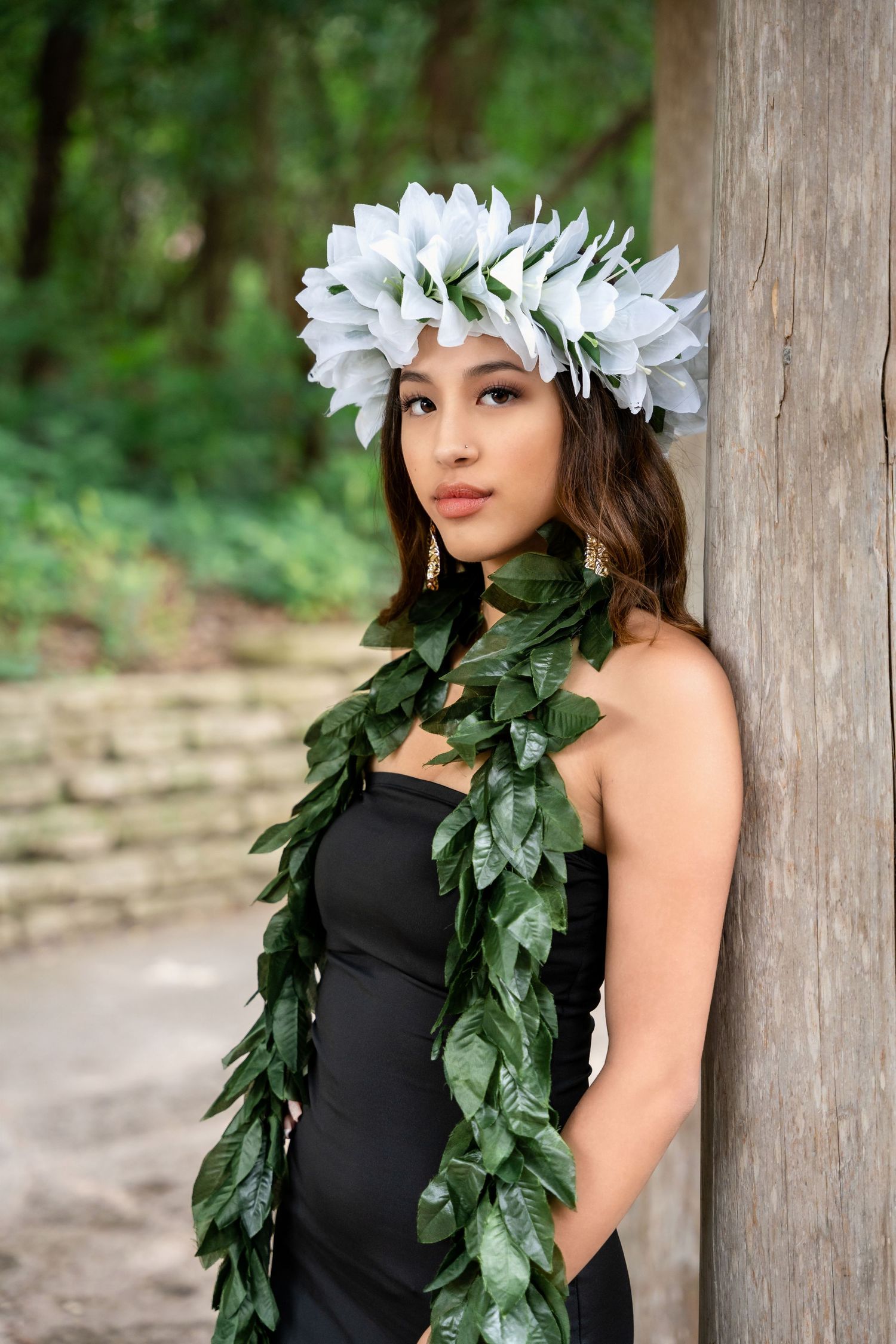Portrait showing white floral crown and green leaf garland against natural garden background.