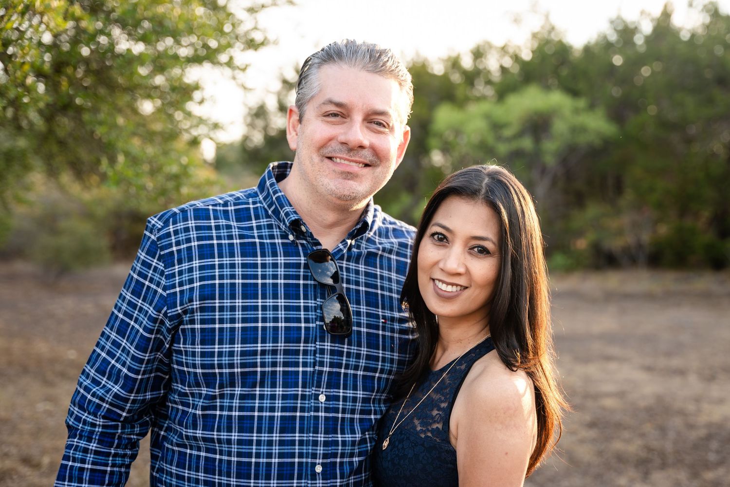 A couple poses outdoors for an engagement photo wearing casual attire.
