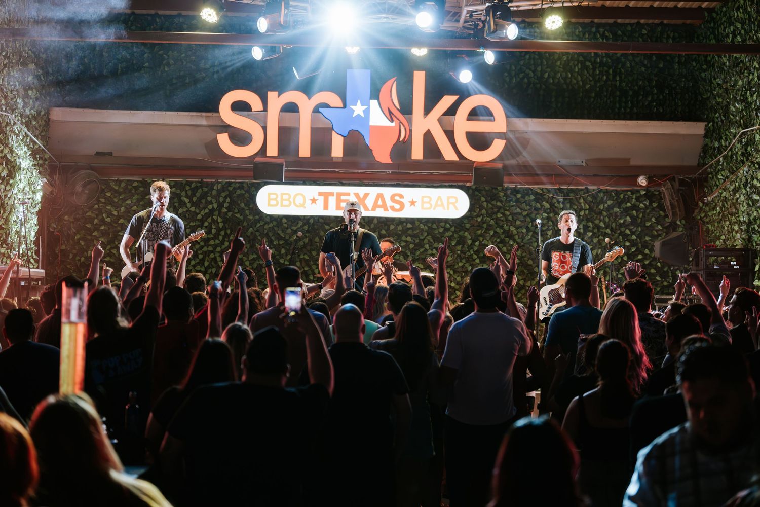 Concert crowd silhouetted against illuminated Smoke venue signage during live performance.