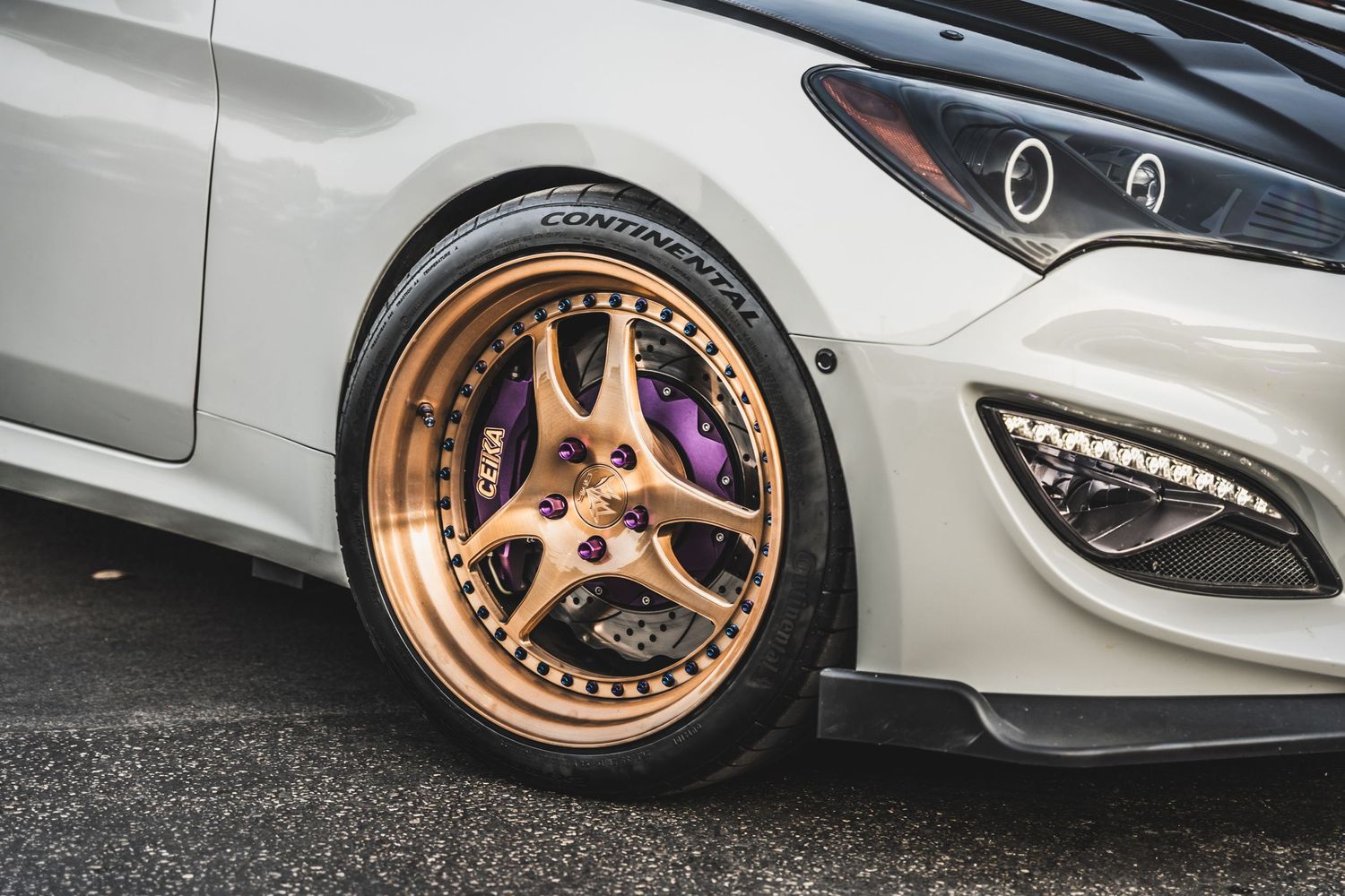 Custom bronze three-spoke wheel with purple brake caliper on silver modern vehicle.