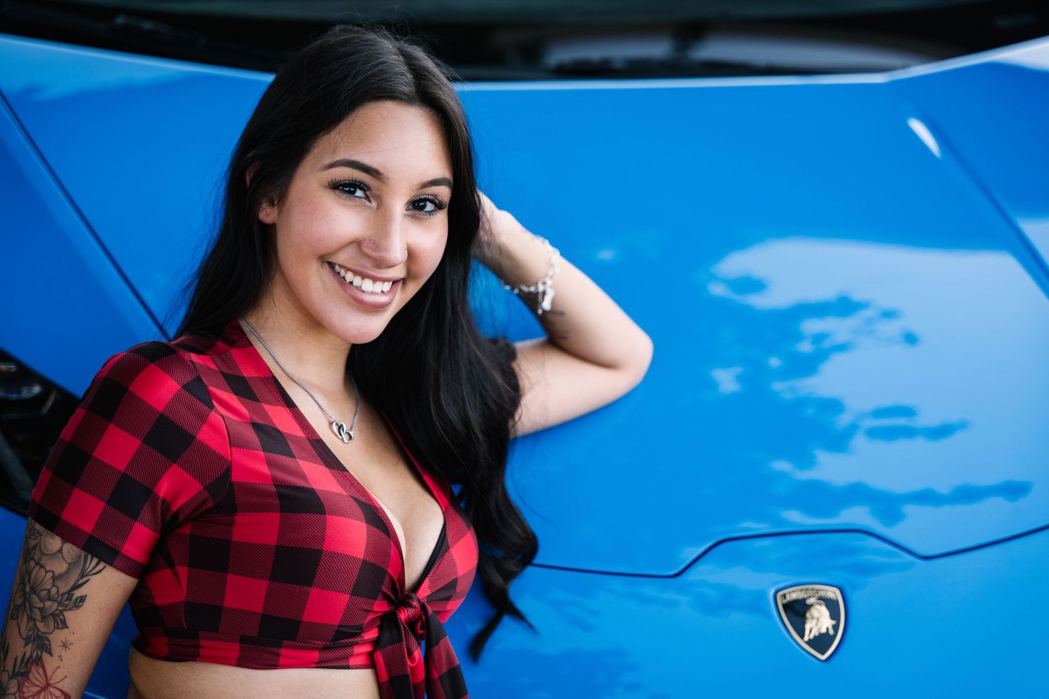 A person in buffalo plaid posing beside a blue Lamborghini with the iconic bull logo visible.