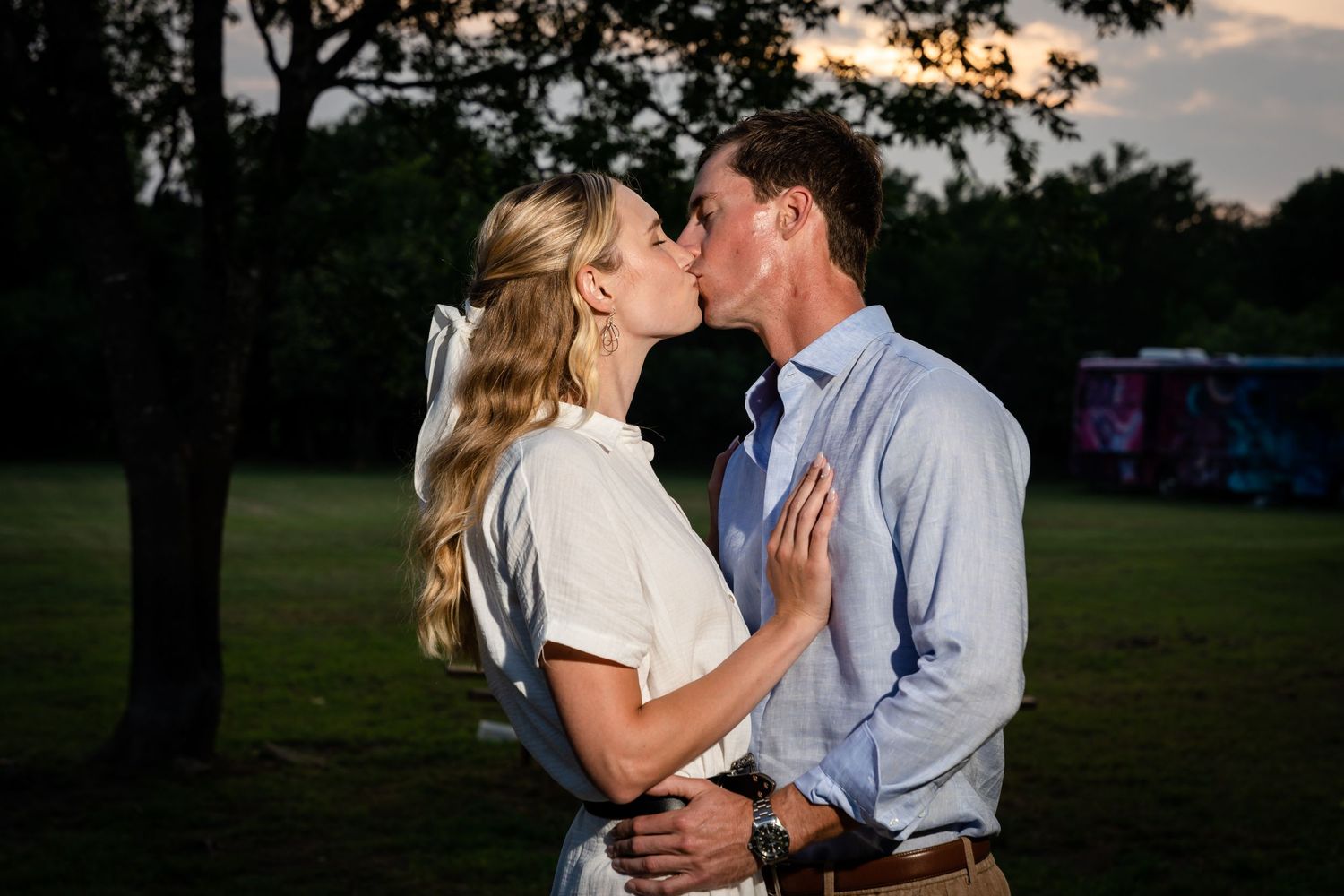 Couple in coordinated outfits share a romantic kiss outdoors at dusk.