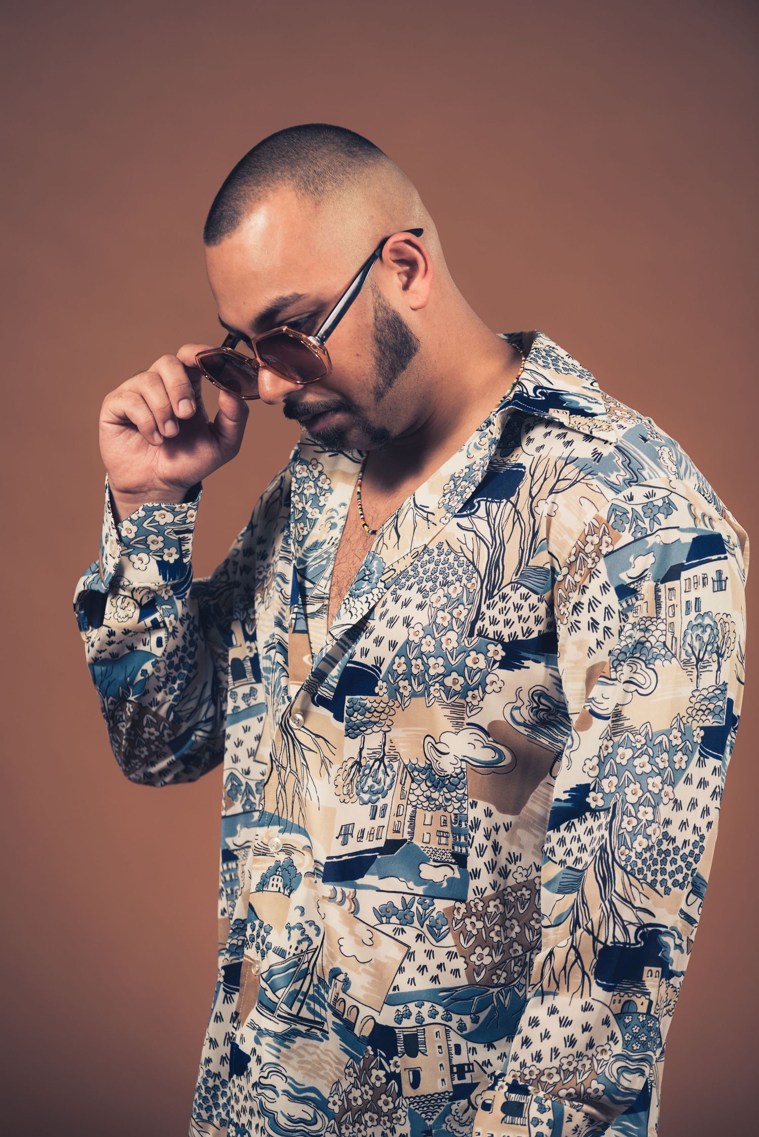 A stylish pattern shirt with blue and white Asian-inspired design worn by a person adjusting their glasses.
