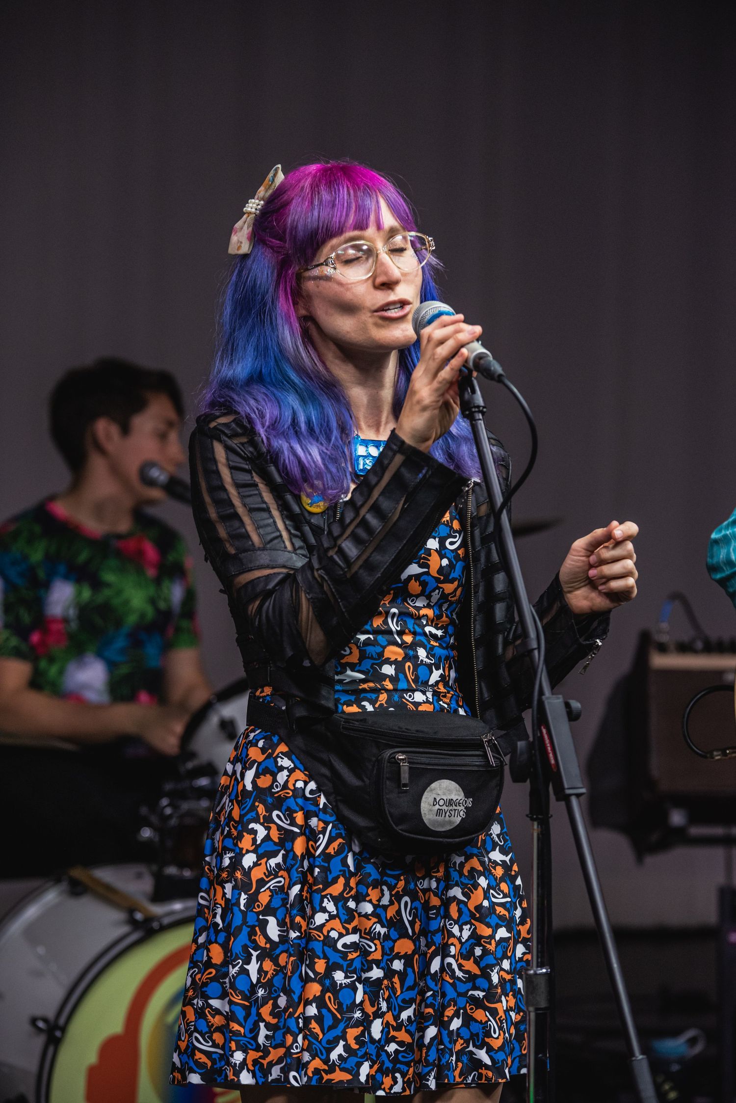 Singer performing on stage wearing colorful dress and vibrant pink and blue hair.