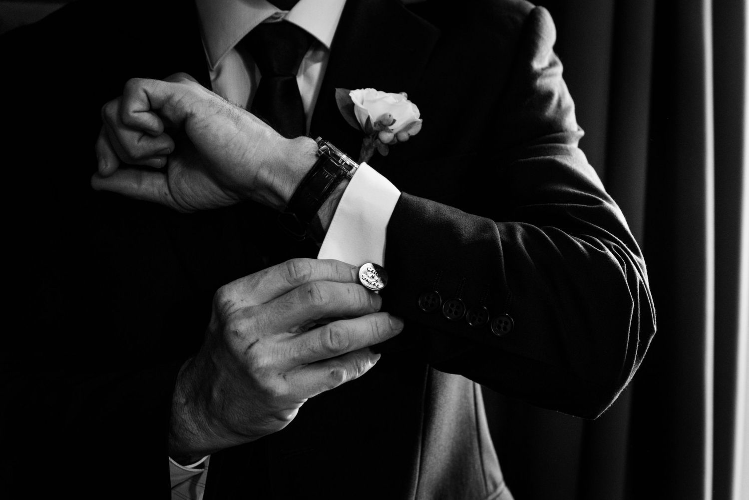 Close-up of hands adjusting formal black suit cuffs and cufflinks.