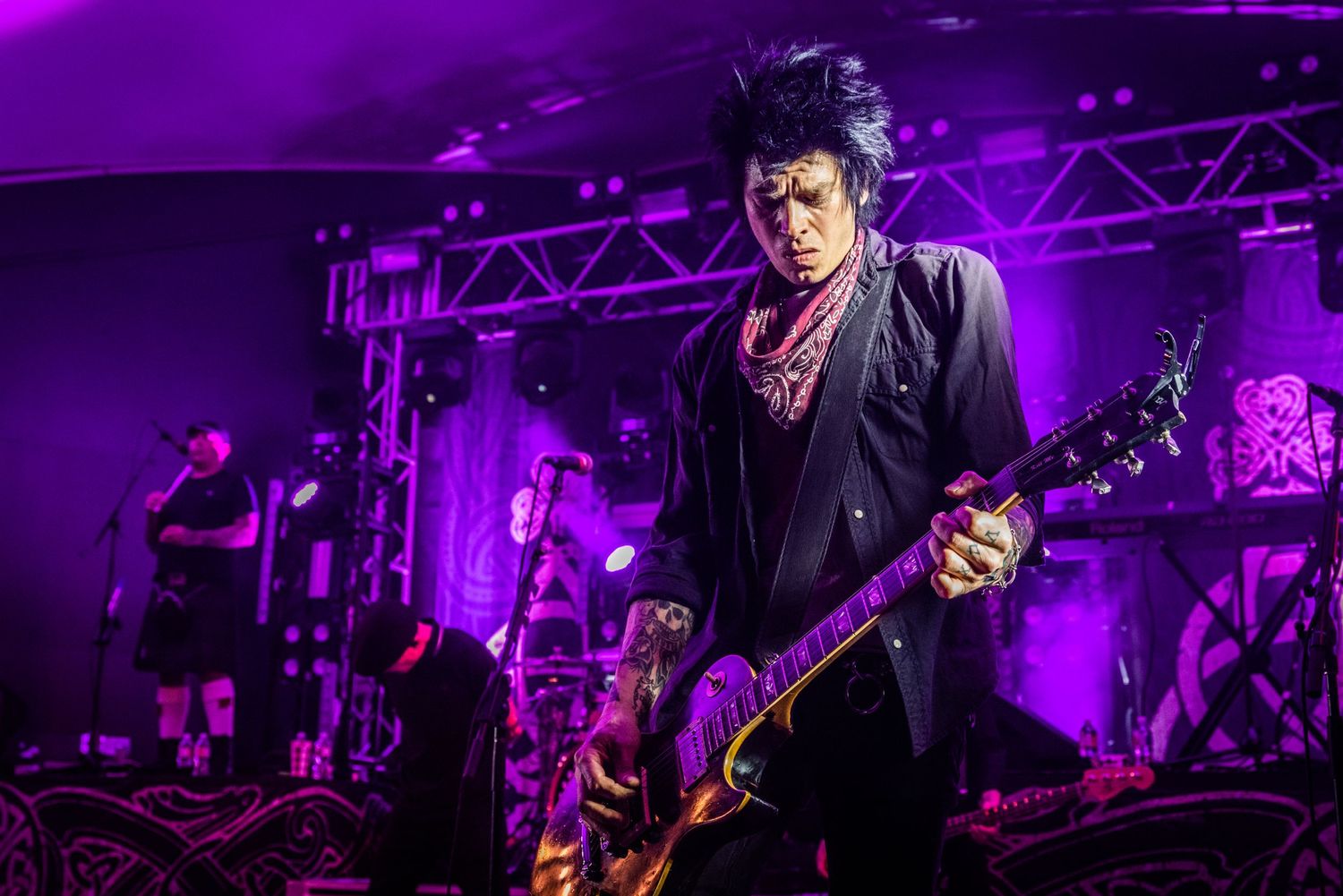 Musician plays electric guitar under dramatic purple stage lighting during an energetic live performance.