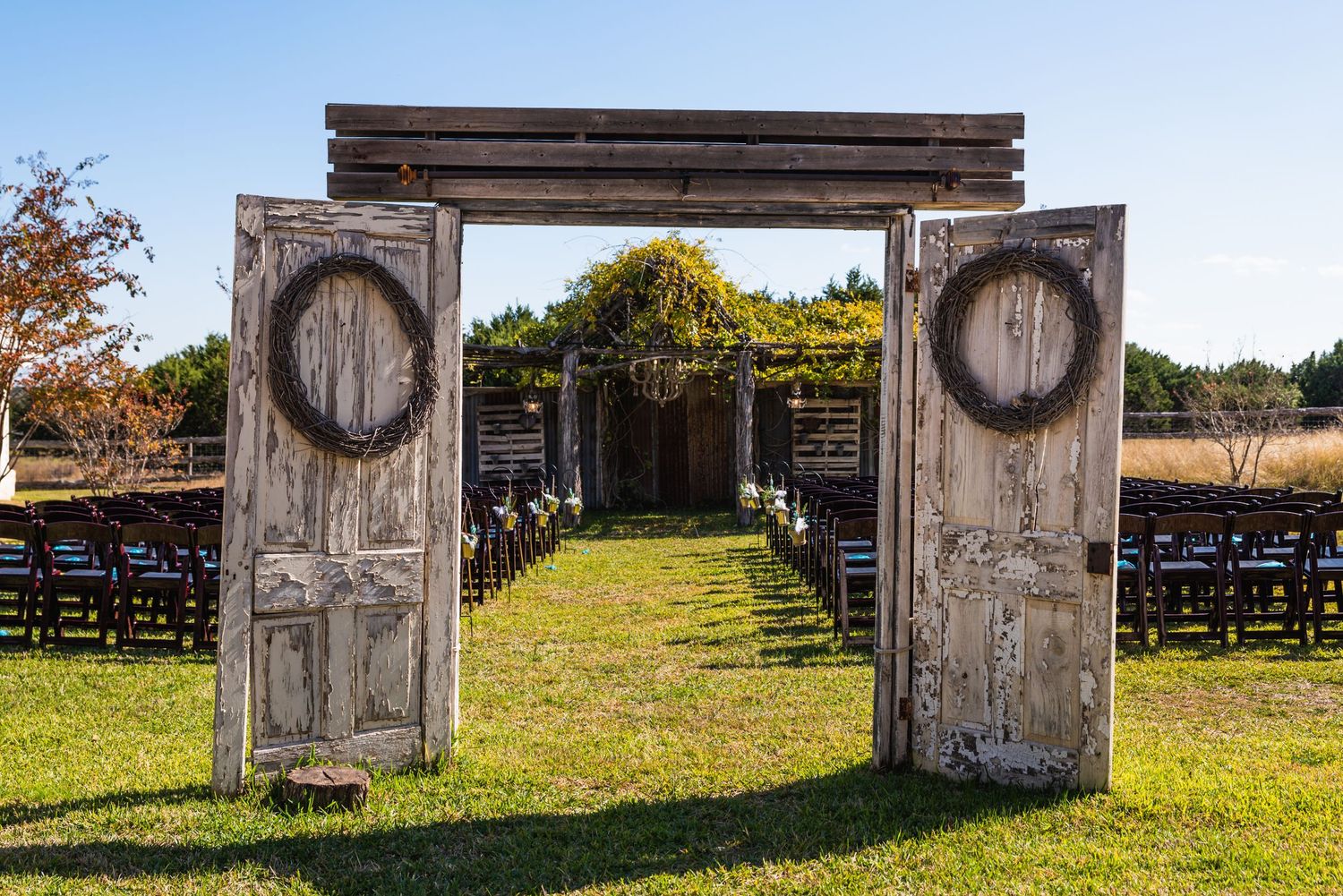 Weathered wooden doors frame outdoor wedding ceremony entrance with rows of chairs.