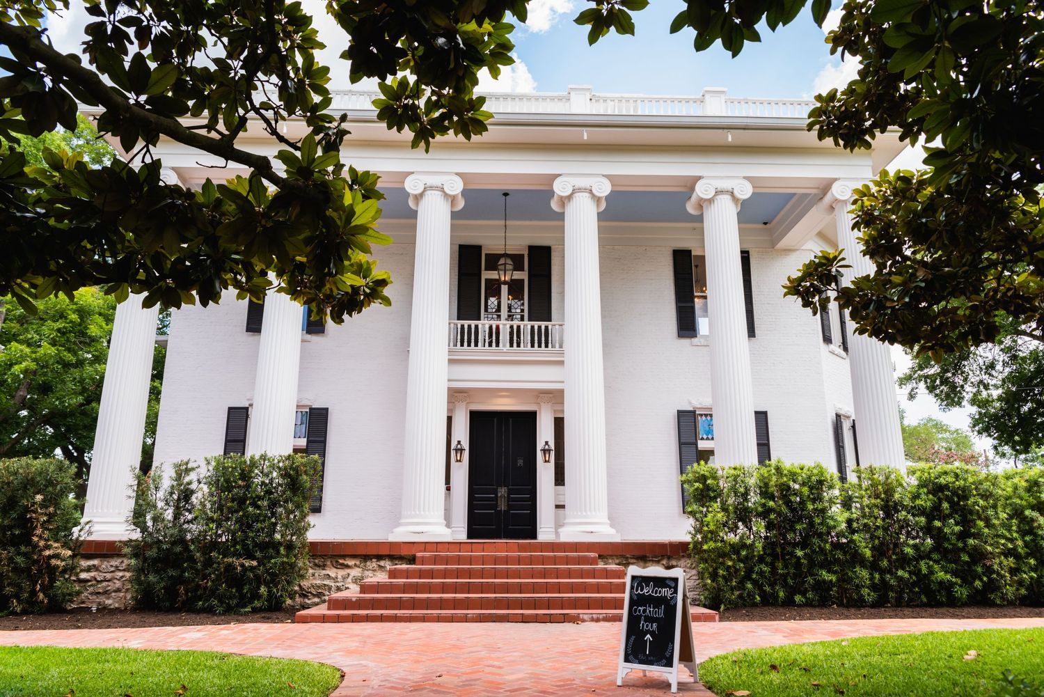 Stately white Southern mansion with tall columns and brick steps leading to black front door.