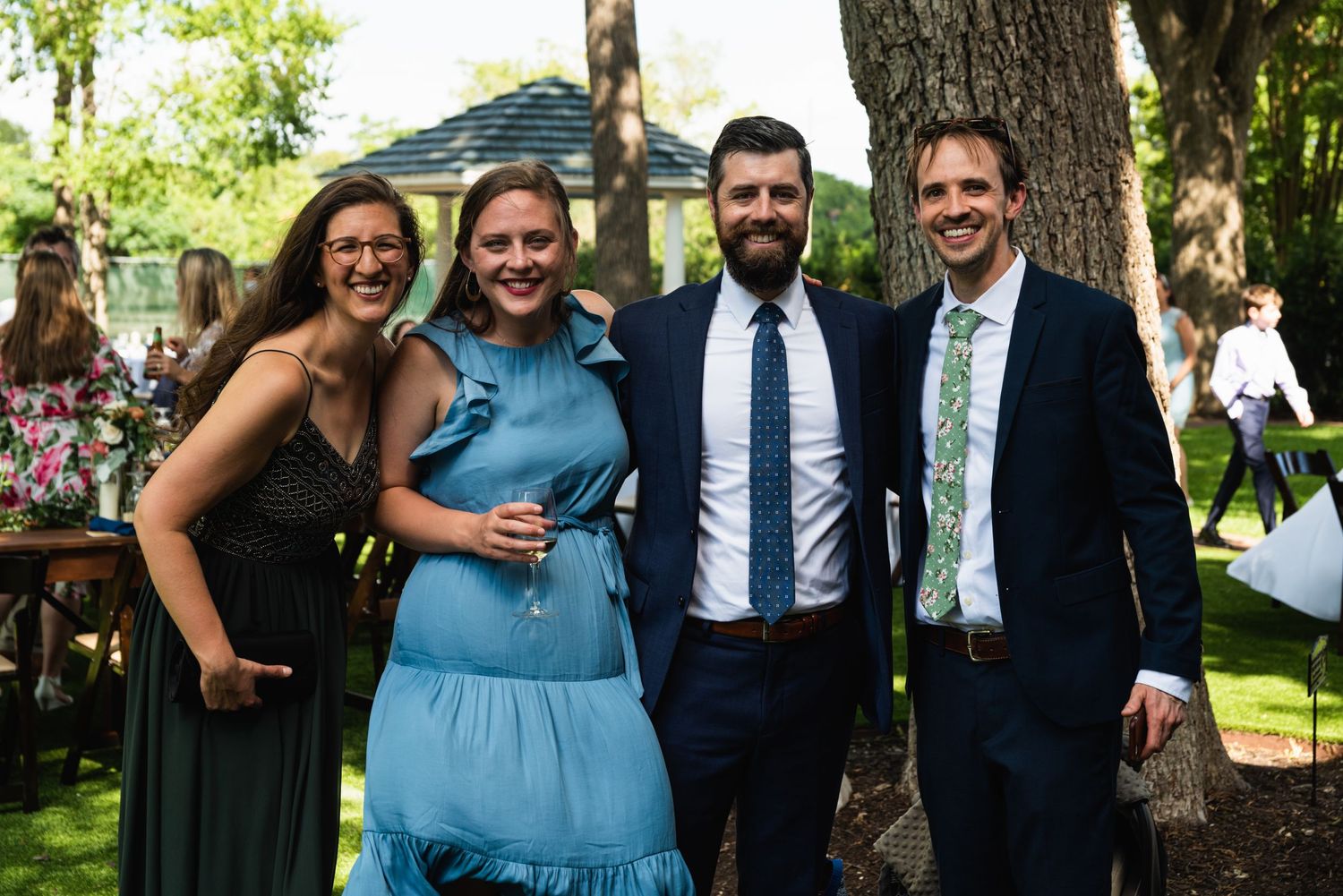 Wedding guests in formal attire pose together at an outdoor garden reception.