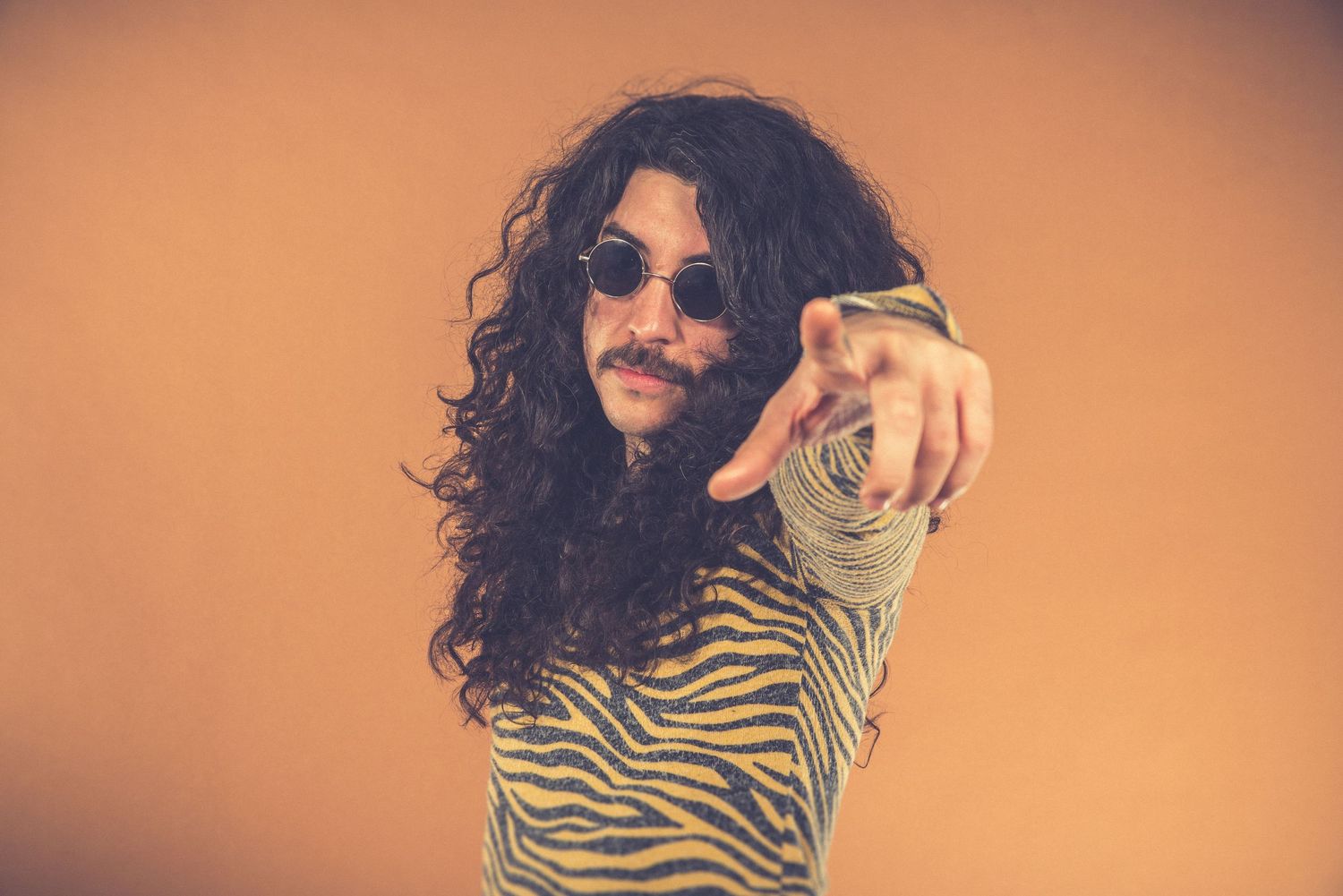 Stylized portrait of person in animal print pointing at camera against orange backdrop.