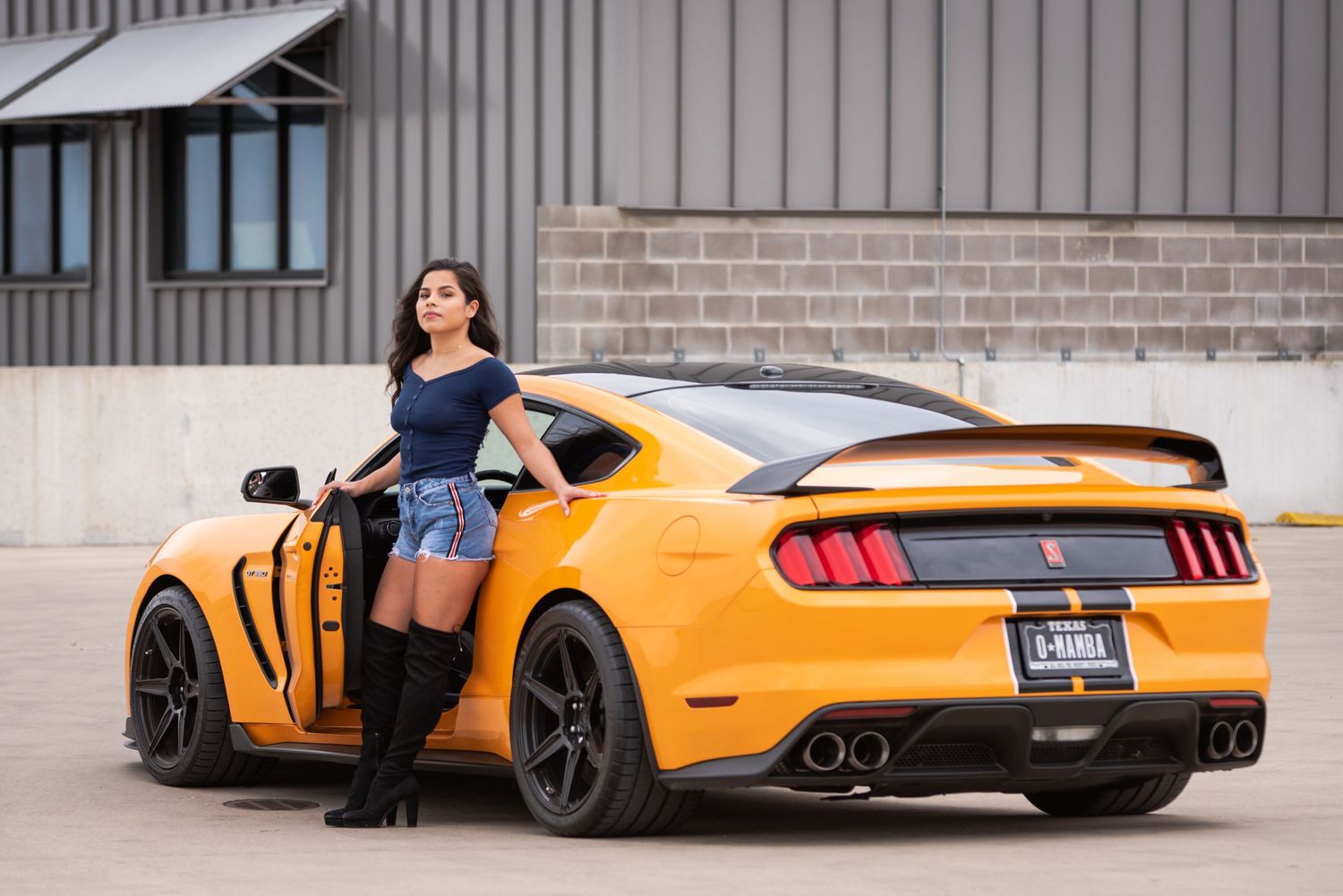 Custom orange Ford Mustang GT350 showcased against industrial building backdrop.