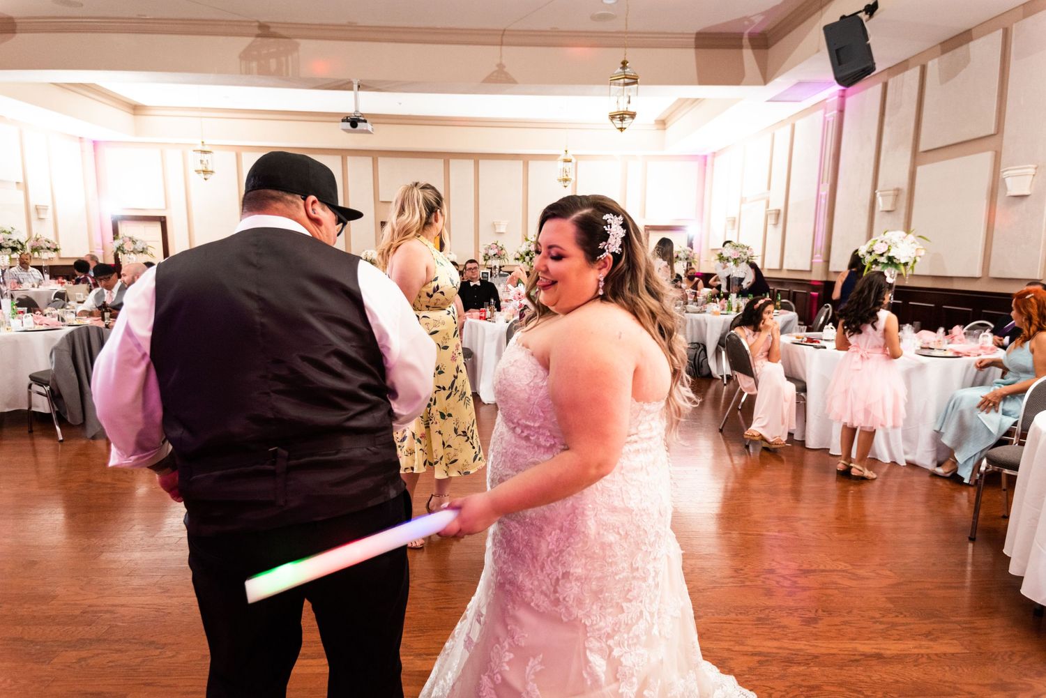 A celebration on the dance floor at a wedding reception with pink ambient lighting.