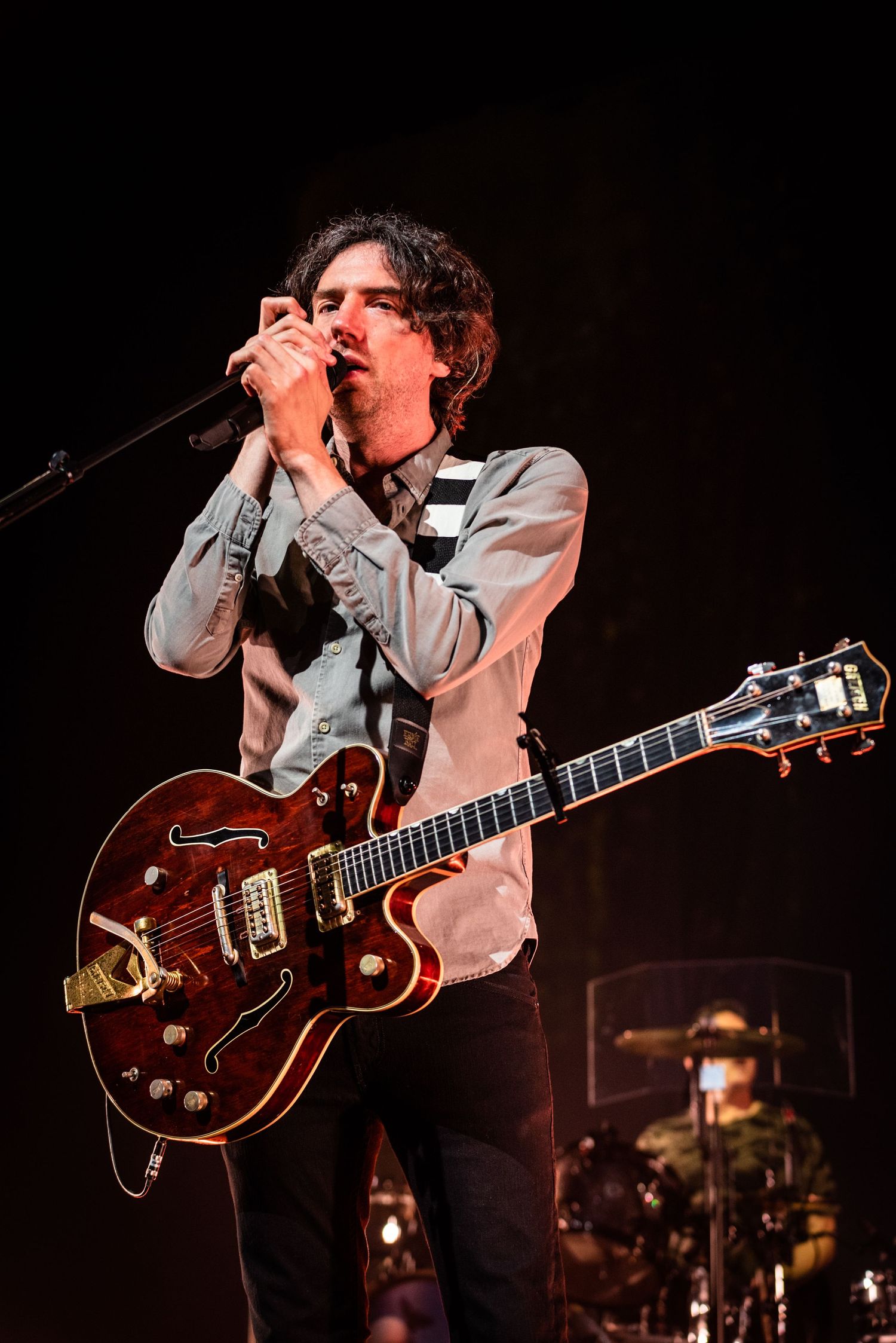 Musician performs with vintage red hollow body guitar wearing checkered vest on concert stage.