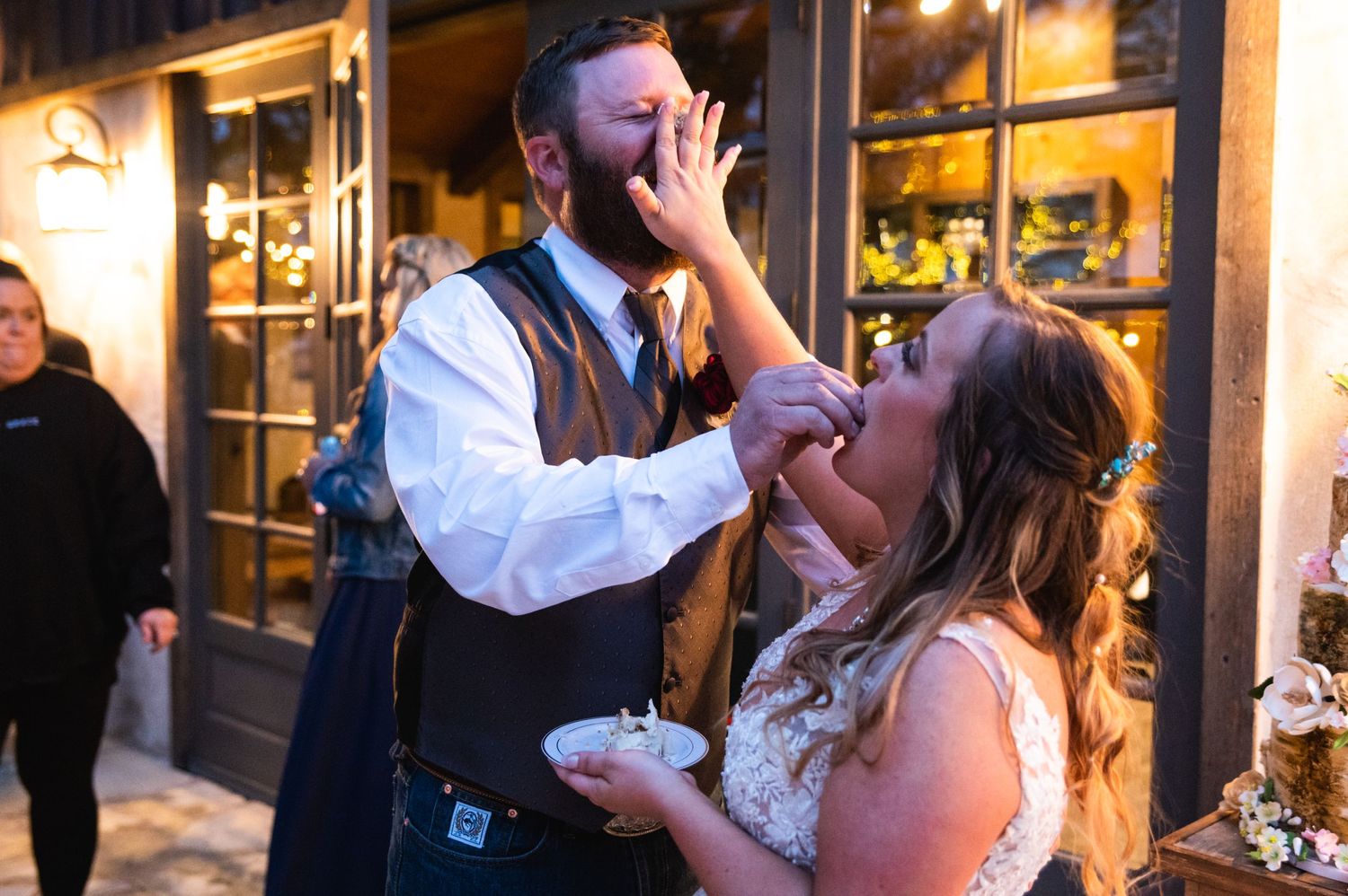 Newlyweds sharing wedding cake and laughing together at their reception.