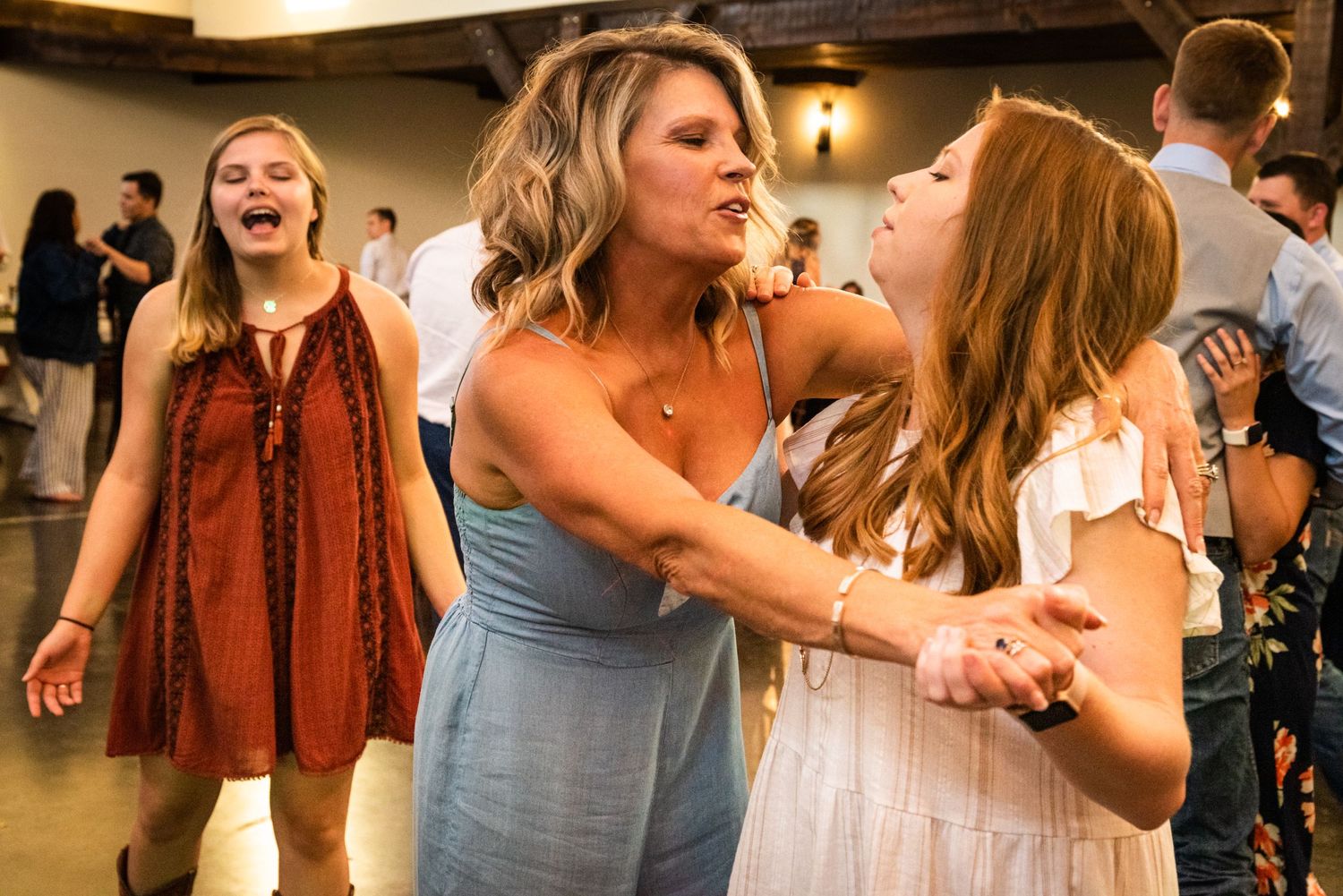 Wedding guests dancing and celebrating with joyful expressions at an indoor reception.