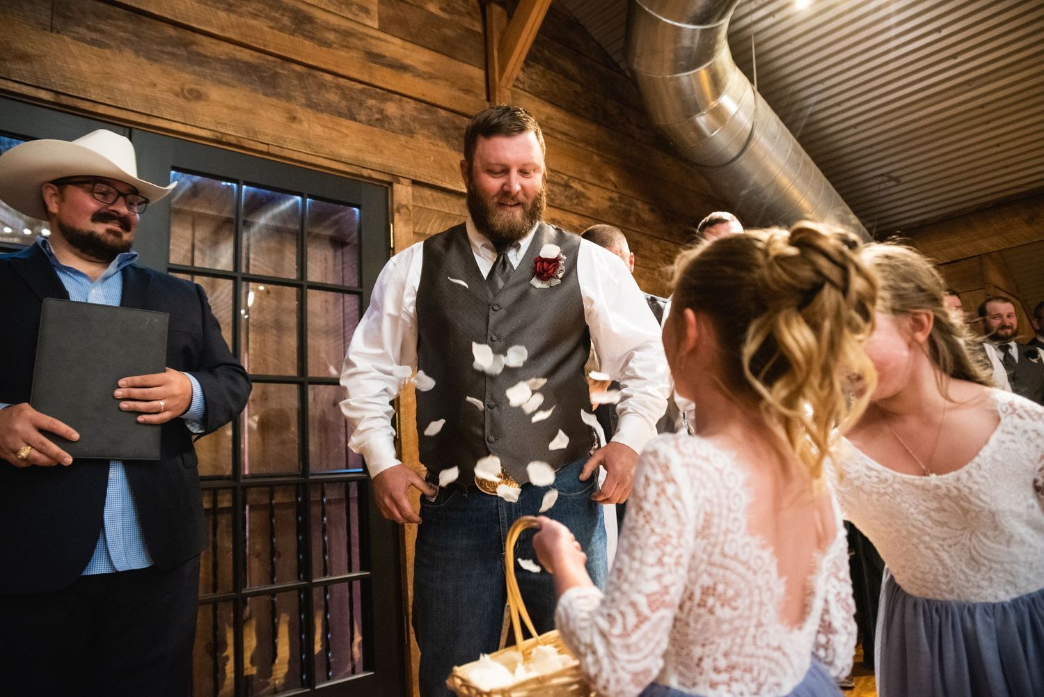 Wedding ceremony participants interact in a rustic barn setting with wooden details.