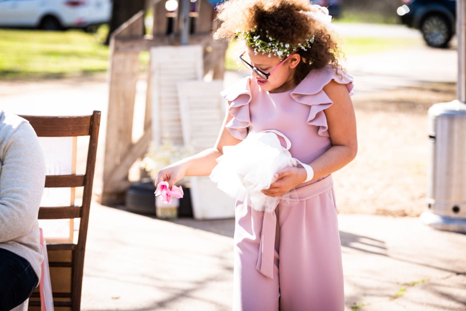 Young attendant in pink dress holding flower basket at outdoor wedding.