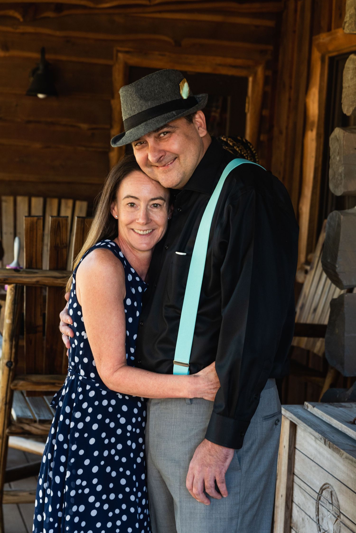 A couple poses in vintage-inspired attire with turquoise suspenders and polka dot dress inside a rustic cabin.