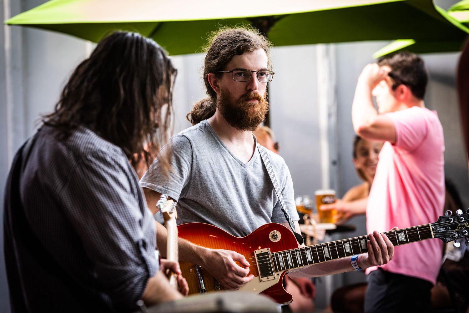 Musicians performing outdoors under green umbrellas with electric guitars.