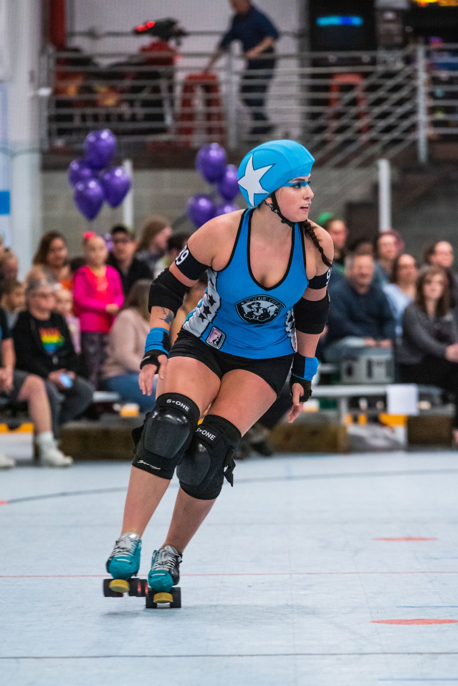 Roller derby player in blue uniform demonstrates skilled skating technique during match.