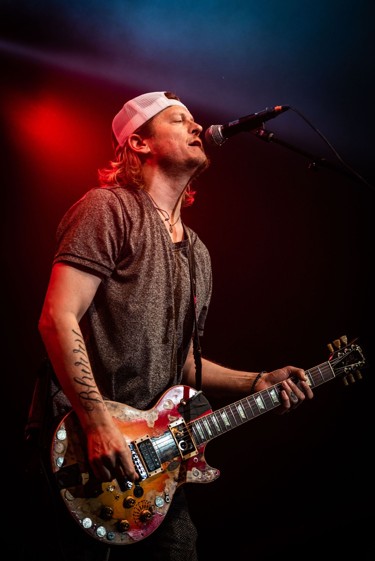 Musician performs on stage with electric guitar in moody red lighting during rock concert.