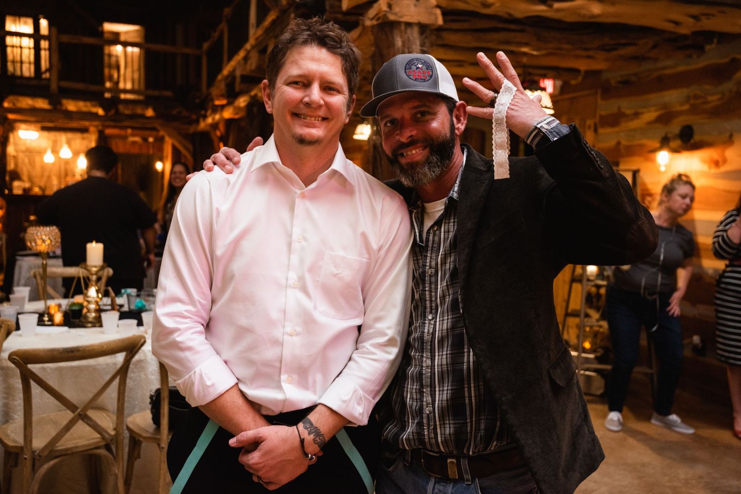 Two guests posing together at a warmly lit rustic wedding reception venue.