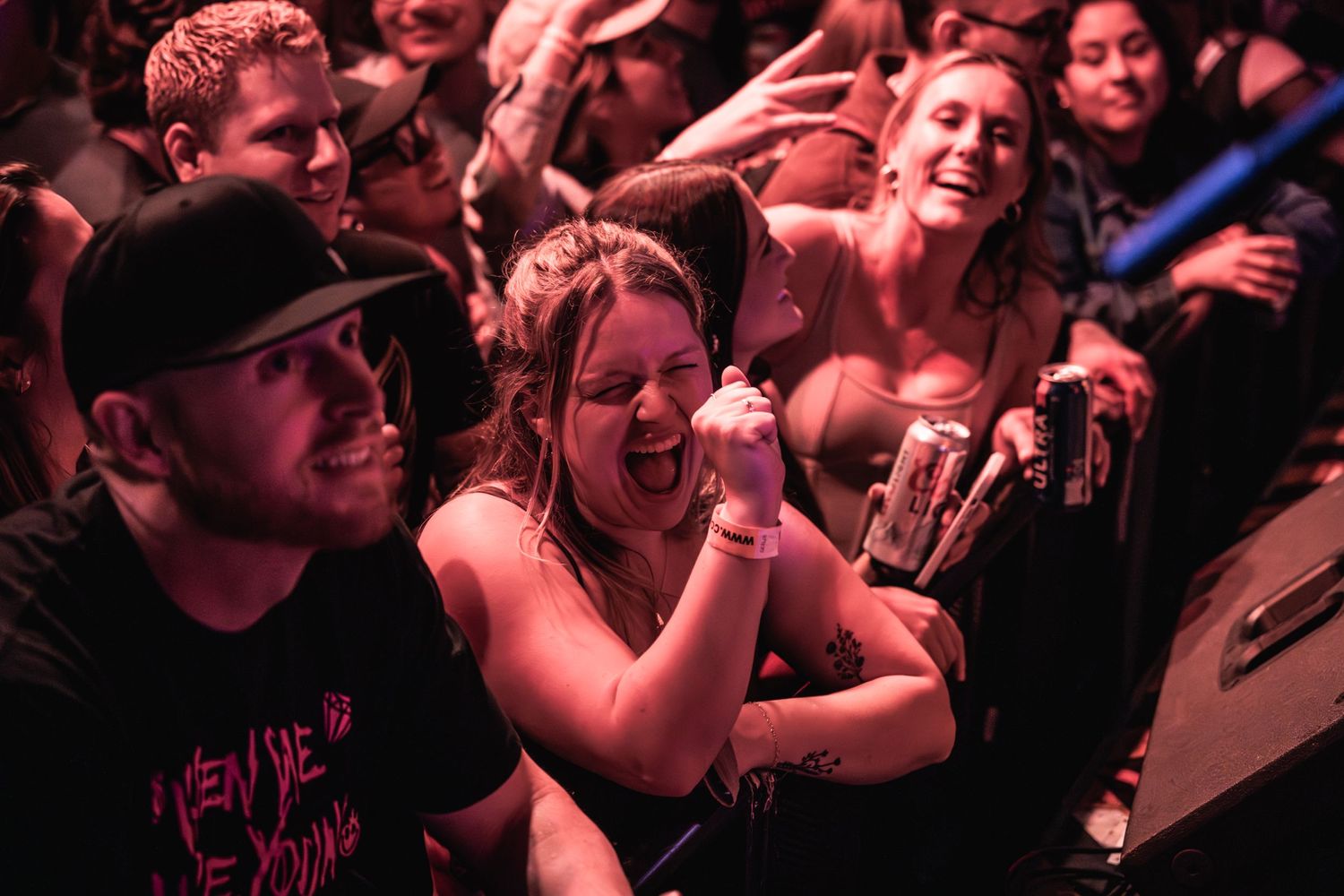 Concert audience bathed in red lighting enjoying live music performance.