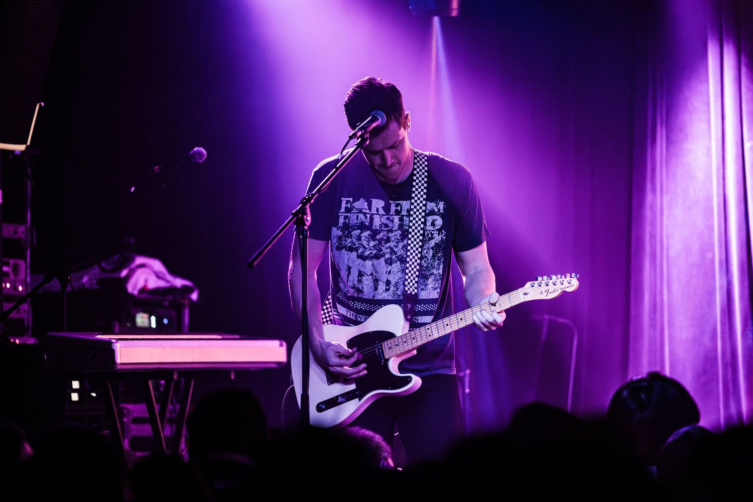 Musician playing guitar under purple stage lights during an intimate concert performance.