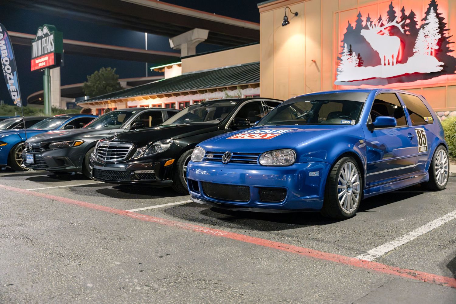 Line of modified cars including a blue VW R32 parked at a nighttime meet.