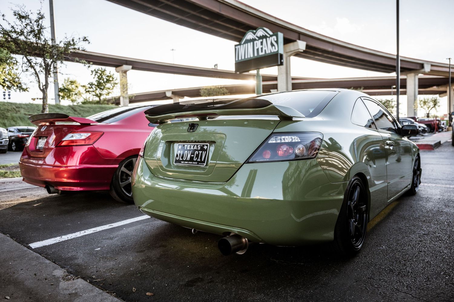 Custom mint green and red sports cars parked under an overpass at a car show.