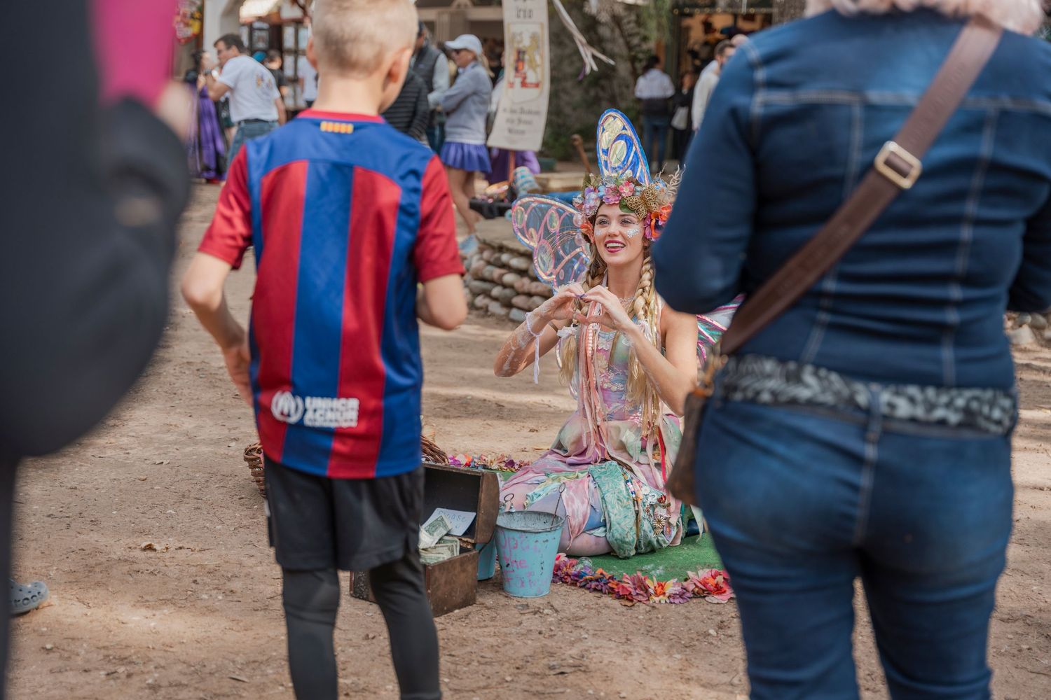 Festival attendees in costume browsing merchandise at an outdoor renaissance fair.